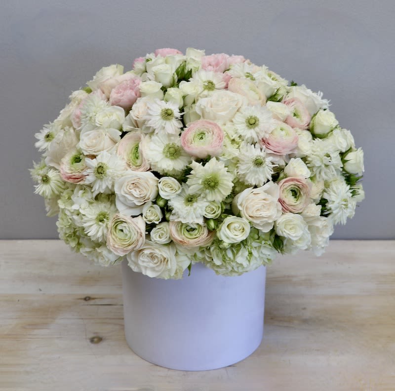 Low round arrangement of white and pale pink flowers in a white cylinder box