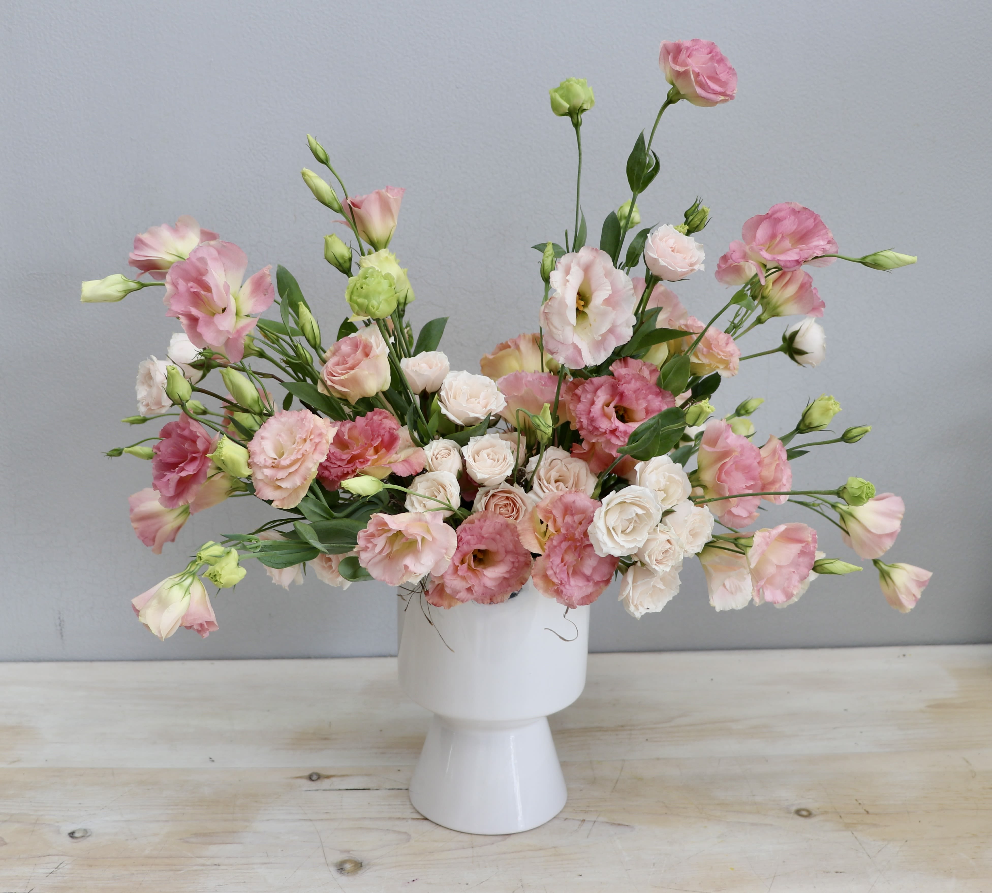 Low wide arrangement of pink lisianthus and blush spray roses in a modern white ceramic vase