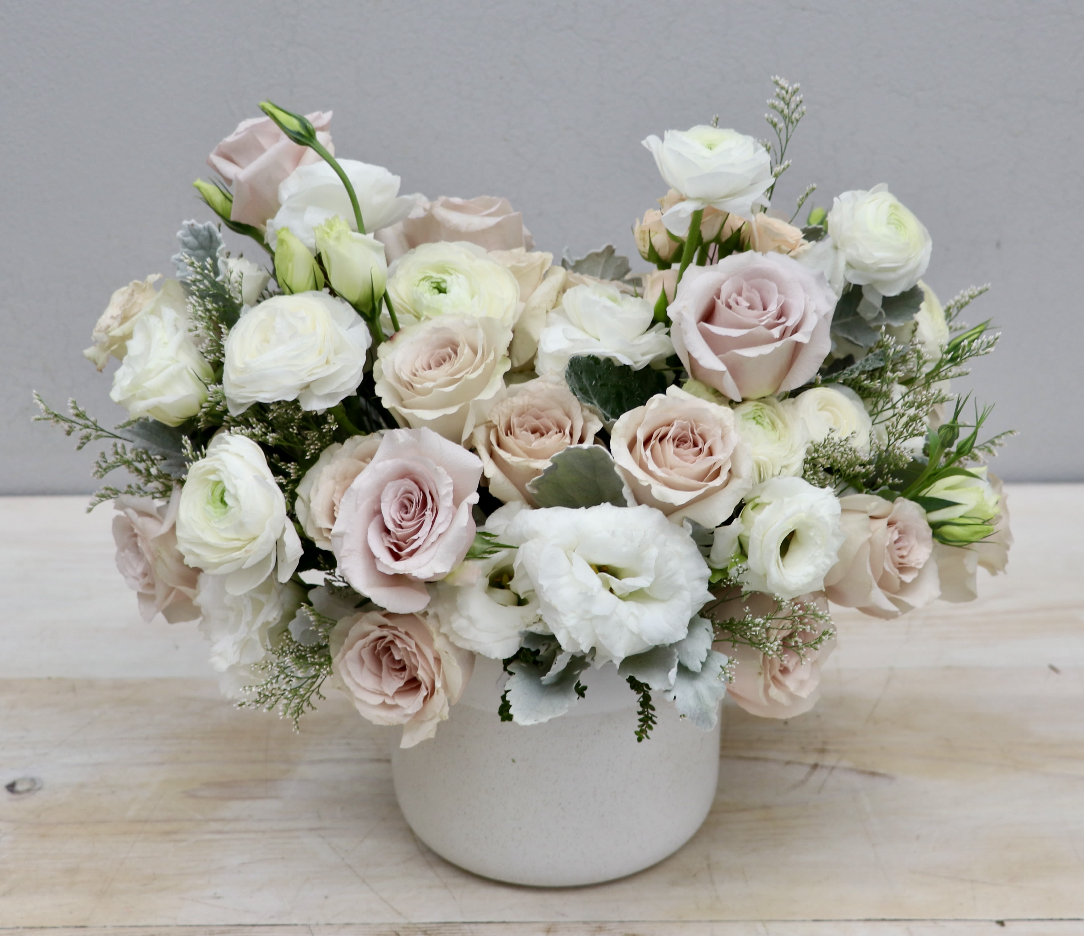 Low arrangement of blush roses and white ranunculus in a matte white ceramic pot