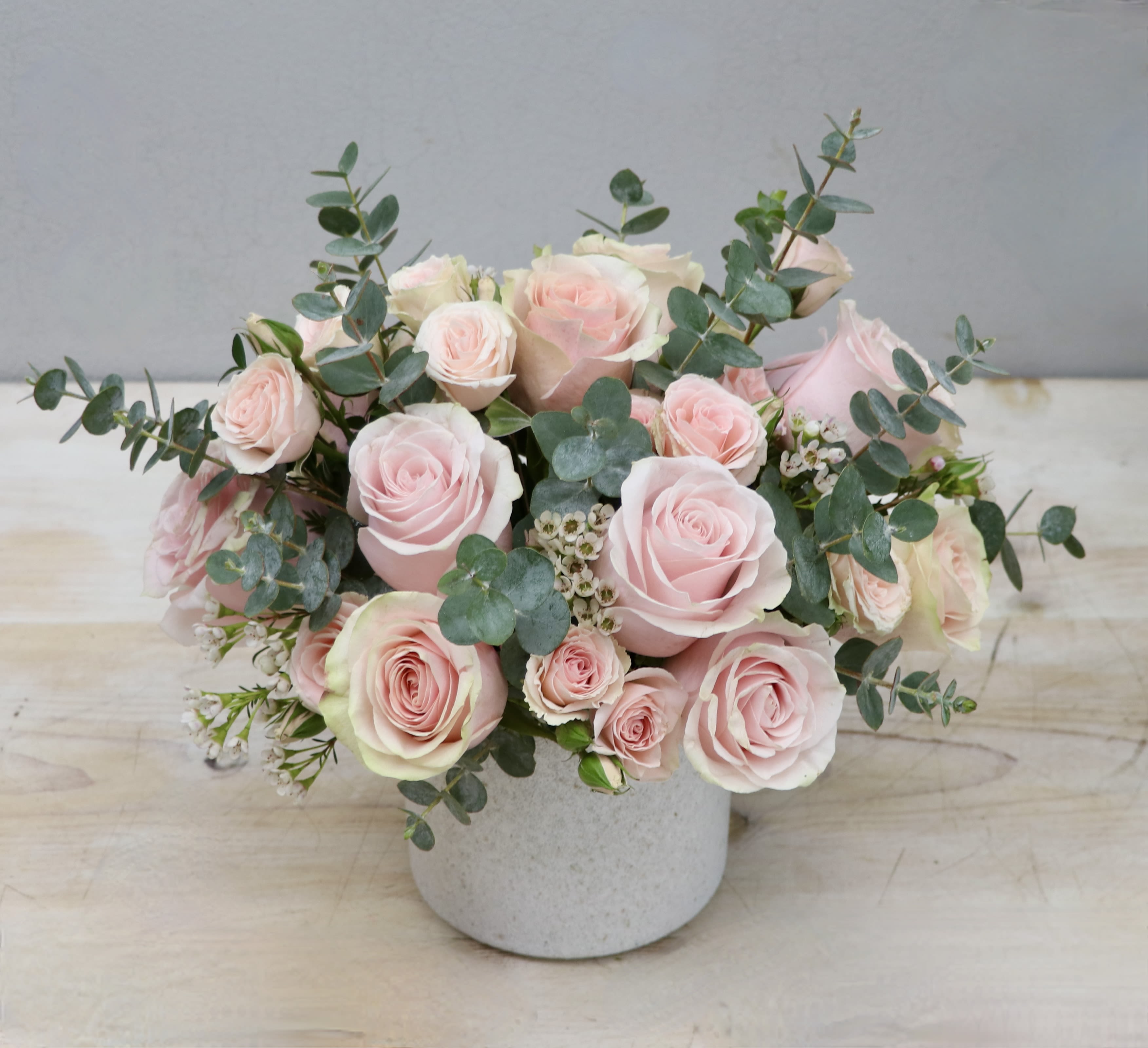 Low arrangement of pale pink roses and spray roses with eucalyptus in a white ceramic vase