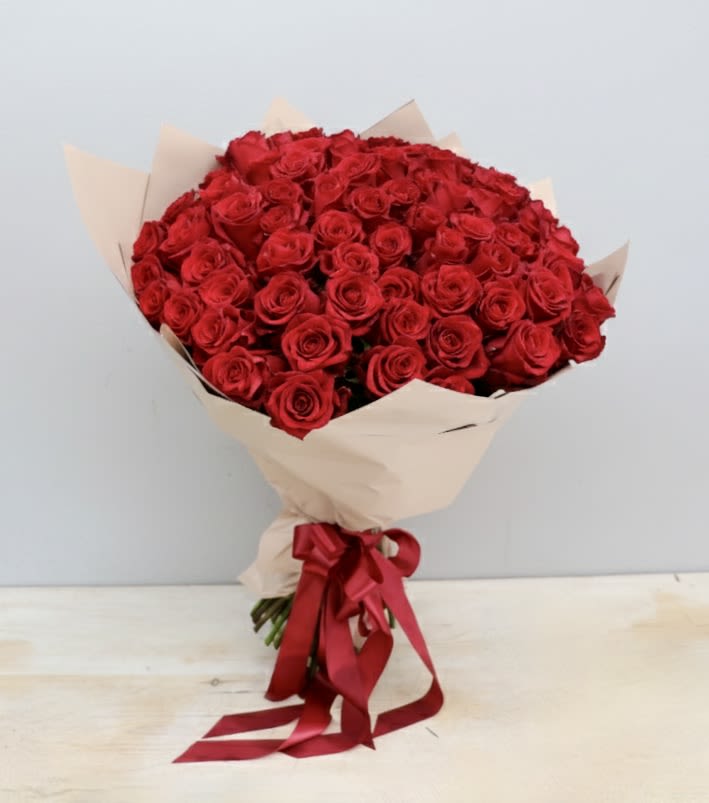 Large bouquet of red roses wrapped in beige paper with a red ribbon bow