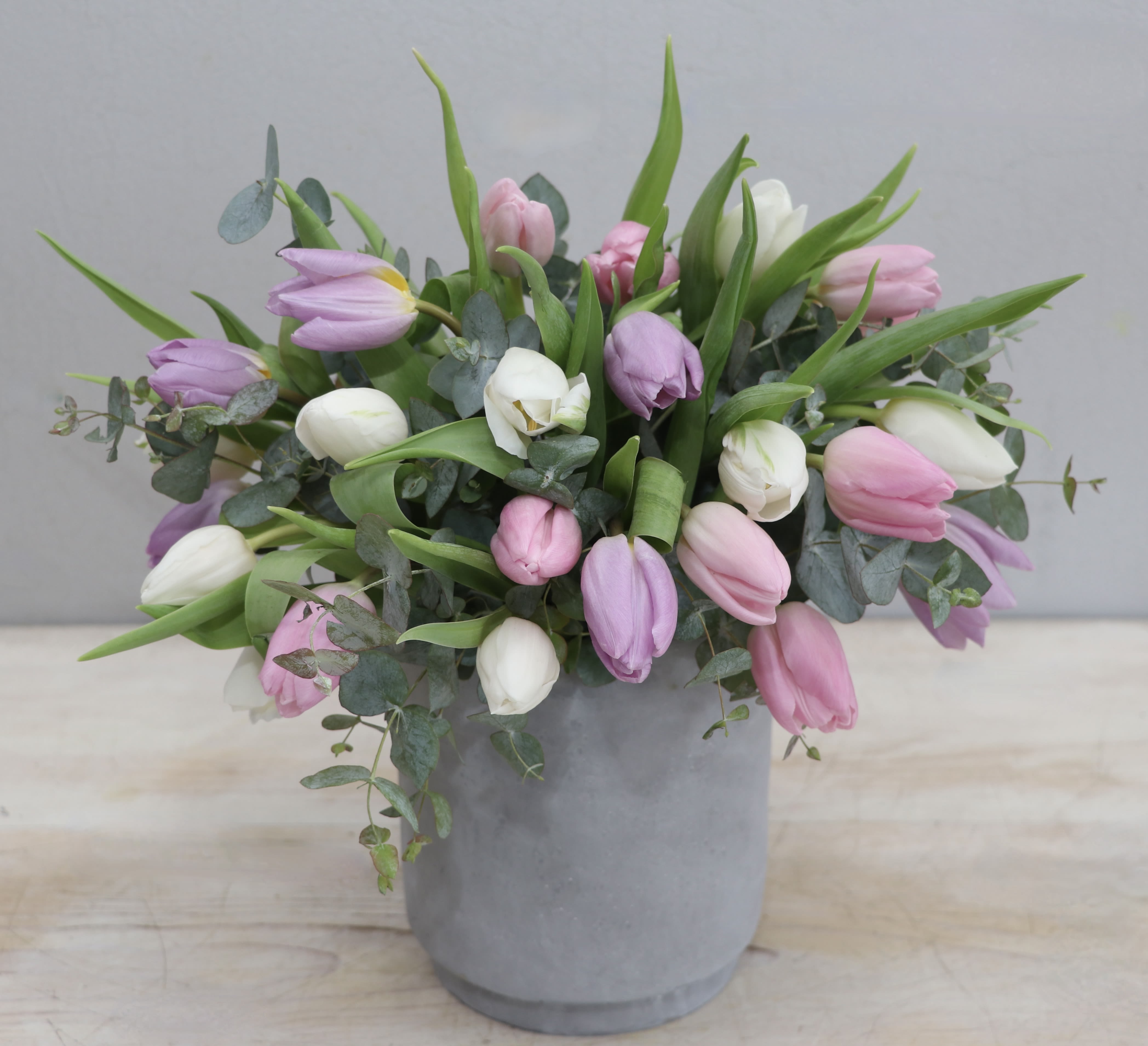 Pastel pink, white, and lavender tulips arranged loosely in a gray pot