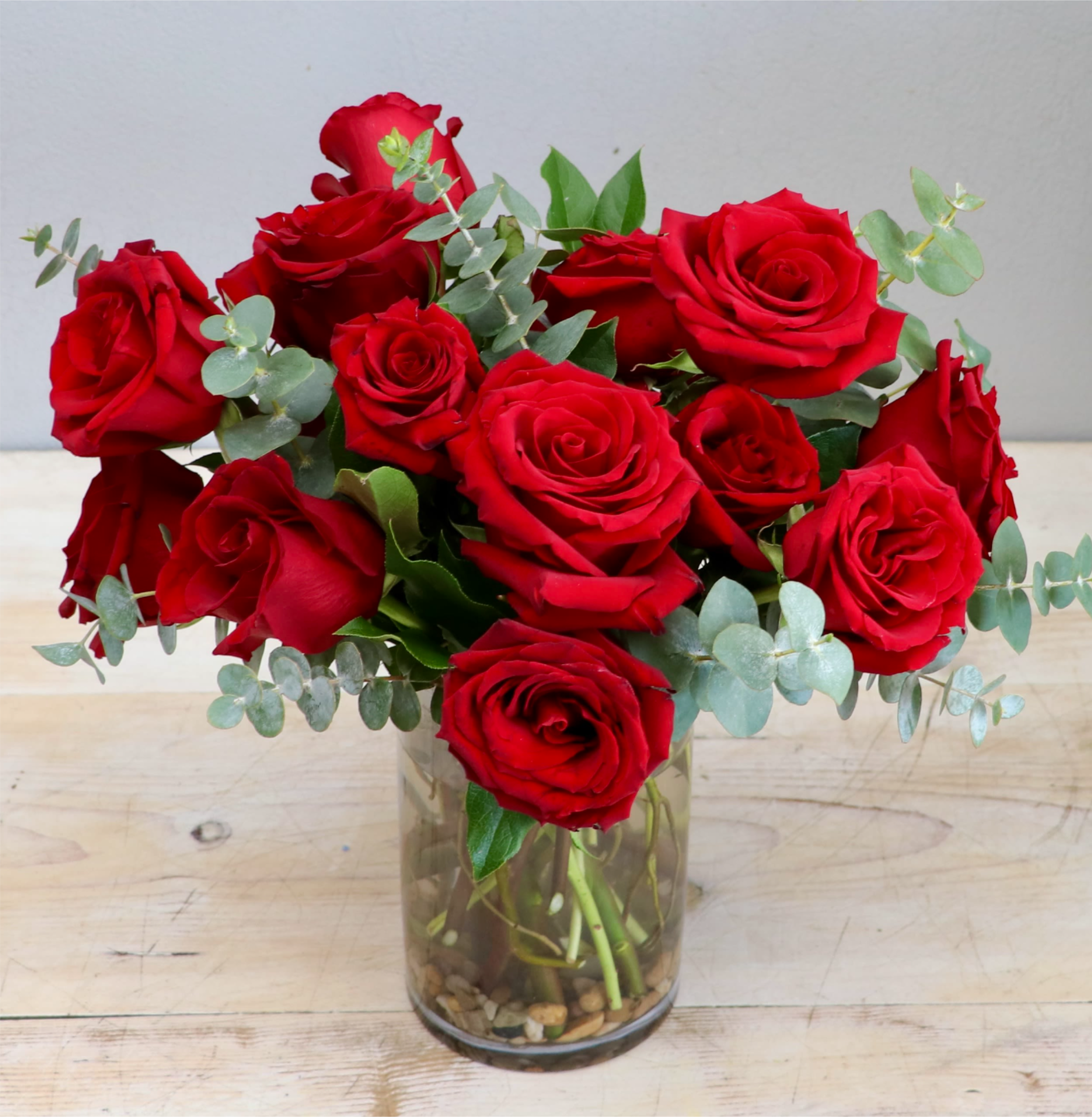 Arrangement of red roses with eucalyptus in a clear glass vase