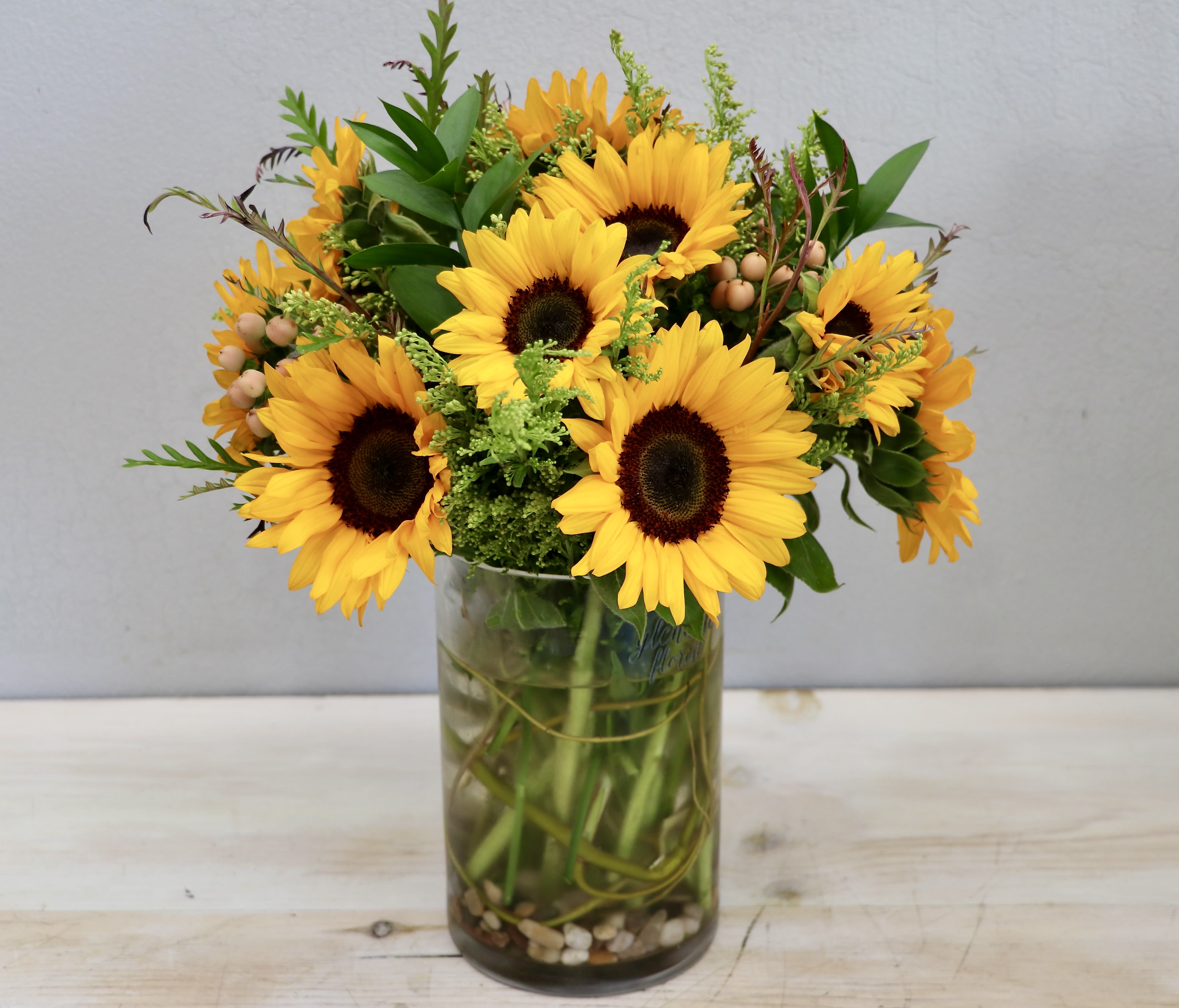 Sunflowers Glee - Glendale Flowers - Sunflowers beautifully arranged in a glass vase with seasonal greenery. Stands approximately 15'' overall.
