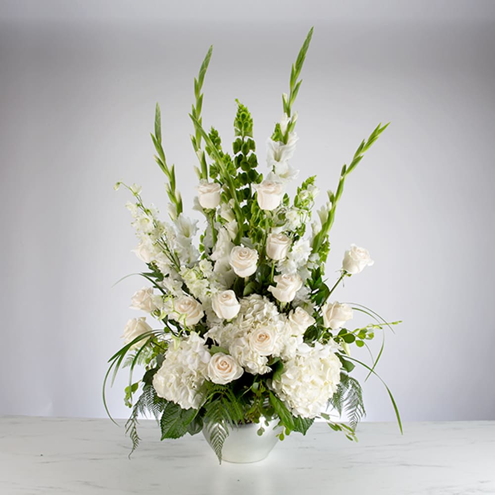 Tall white arrangement with roses, hydrangeas, and green Bells of Ireland in a white bowl vase