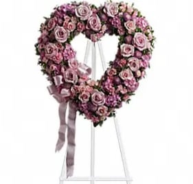Heart-shaped pink rose wreath on a white stand with ribbon