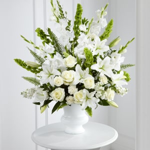Morning Stars Arrangement  - The FTD® Morning Stars™ Arrangement is a brilliant expression of peace and soft serenity. White roses, carnations, gladiolus, stock, and Oriental lilies are accented with the bright green stems of Bells of Ireland and a gorgeous assortment of lush greens, while seated in a white designer plastic urn to create a beautiful way to honor the life of the deceased. 