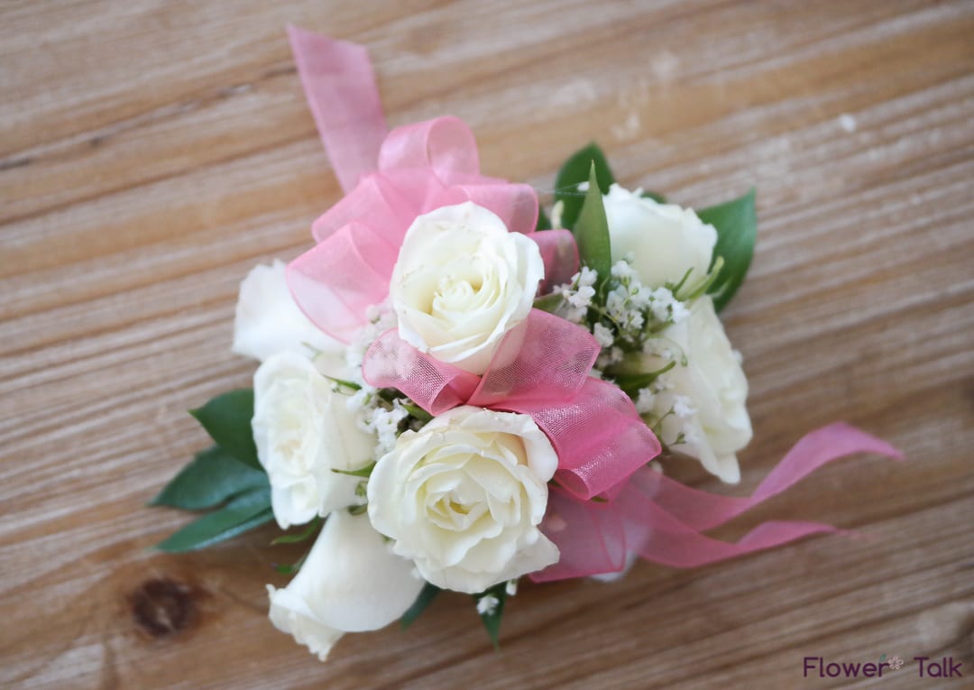 White rose corsage with pink ribbon on a wooden surface