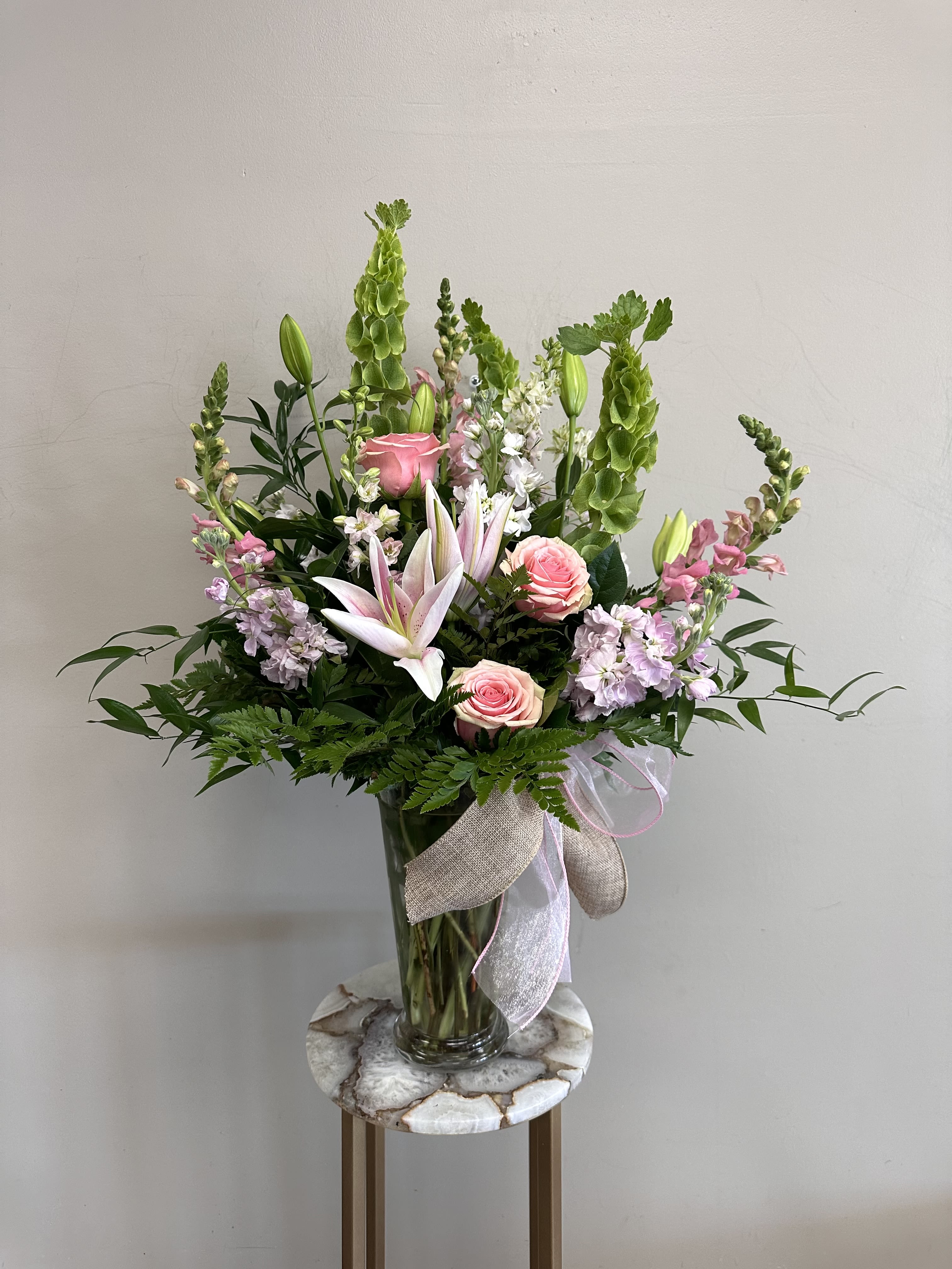 Pink lilies and roses in a glass vase with green spikes