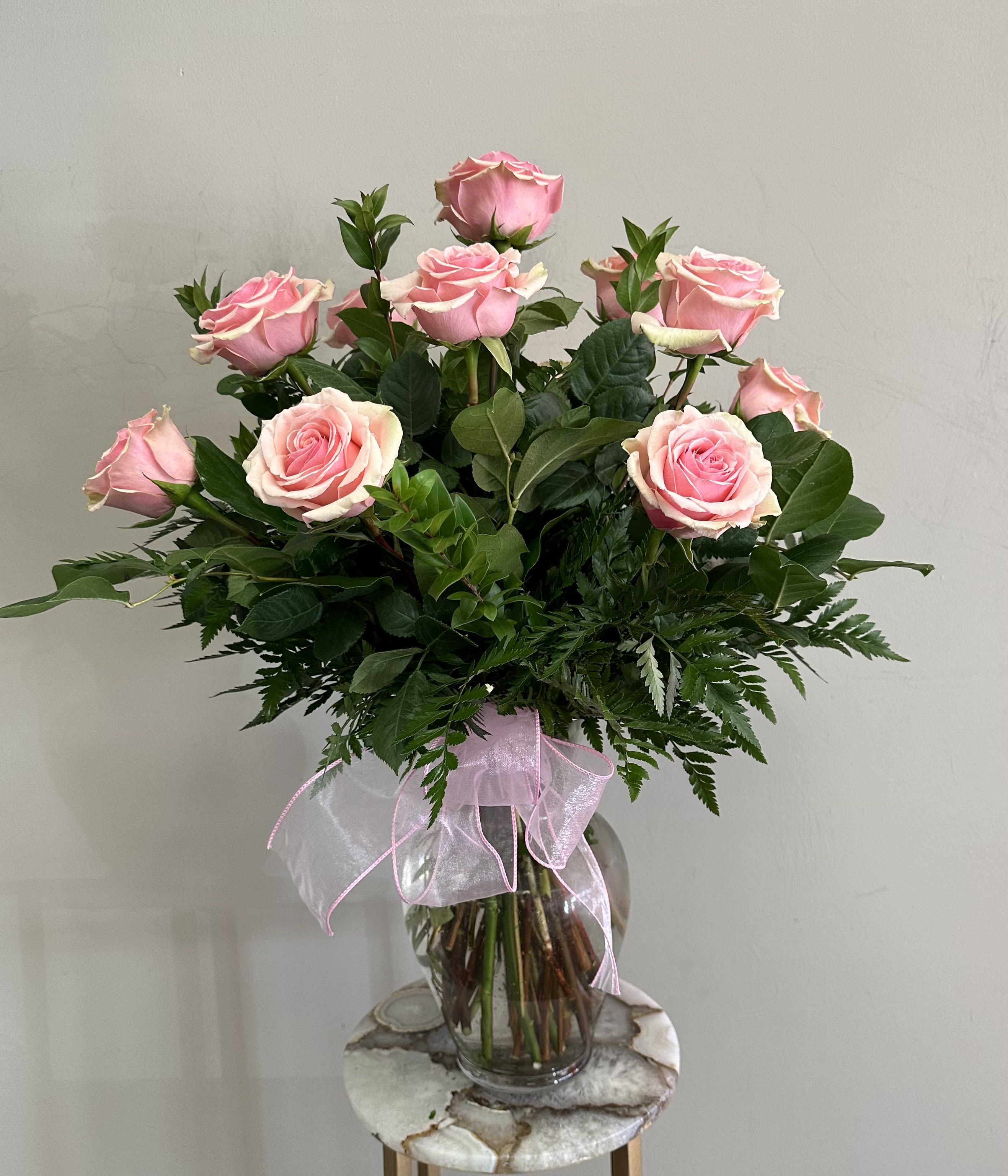 Pink roses arranged in a clear glass vase with a pink ribbon bow