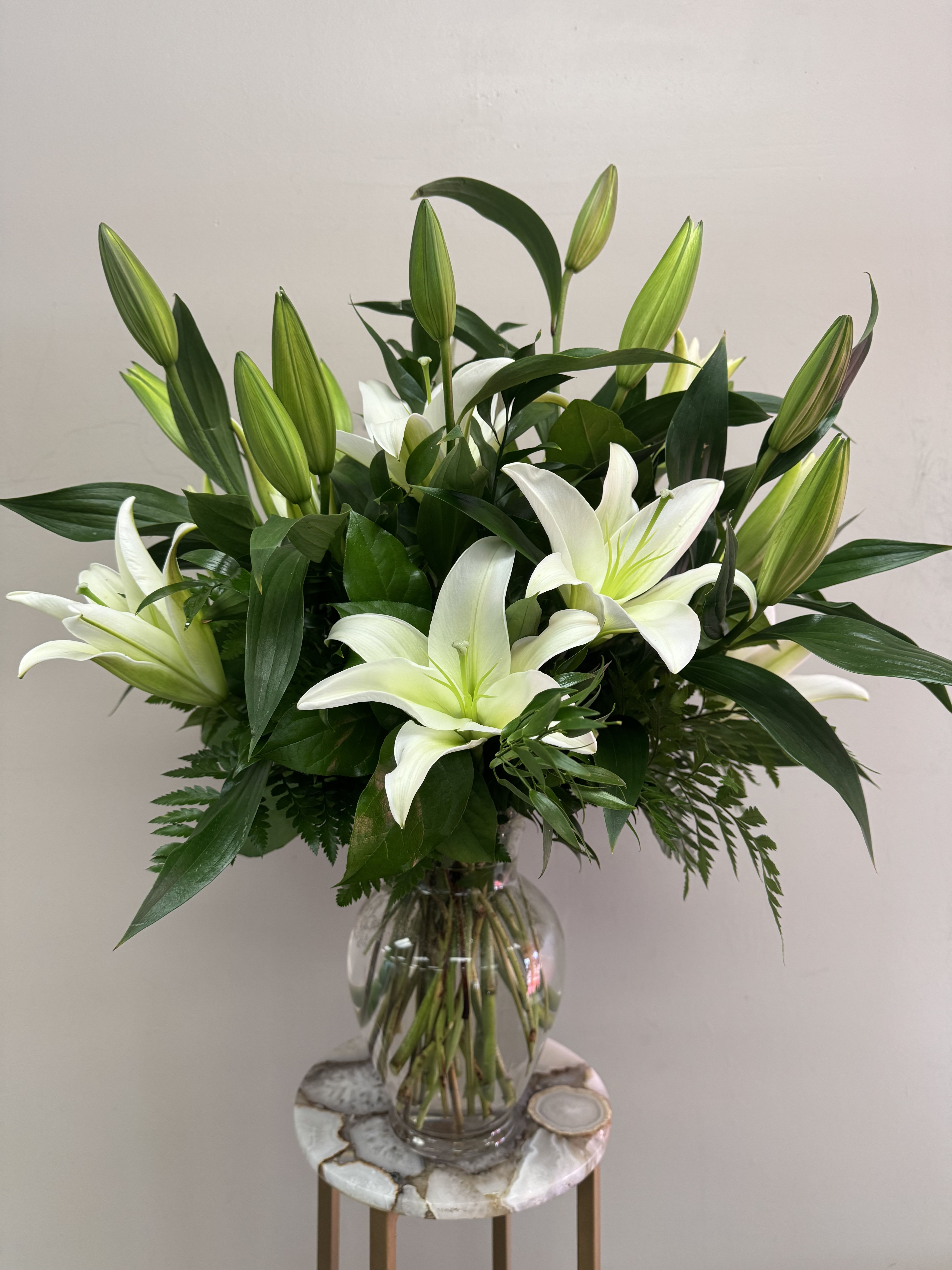 Tall arrangement of white lilies with green buds in a clear glass vase.