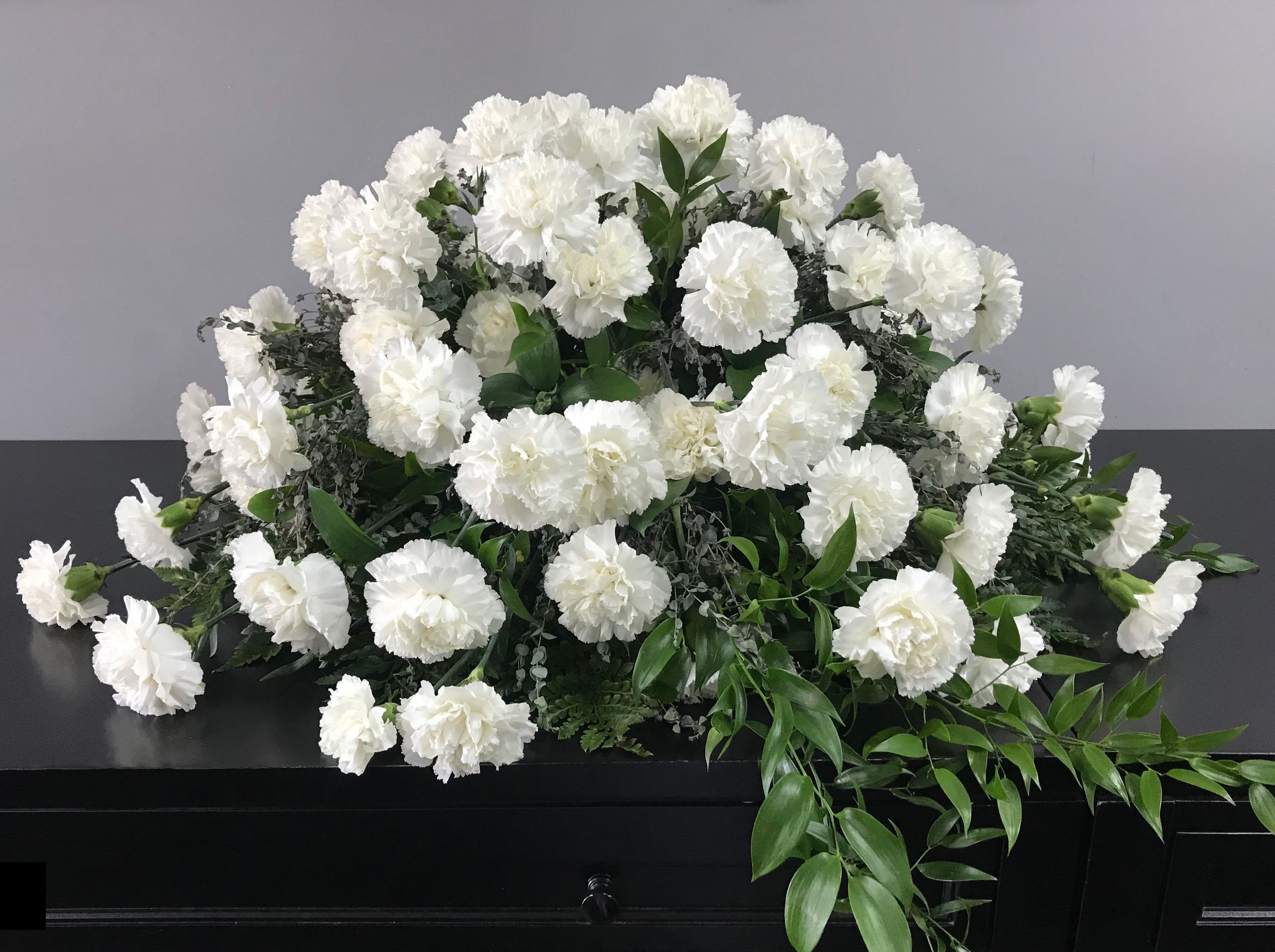 White carnation funeral spray on a dark casket
