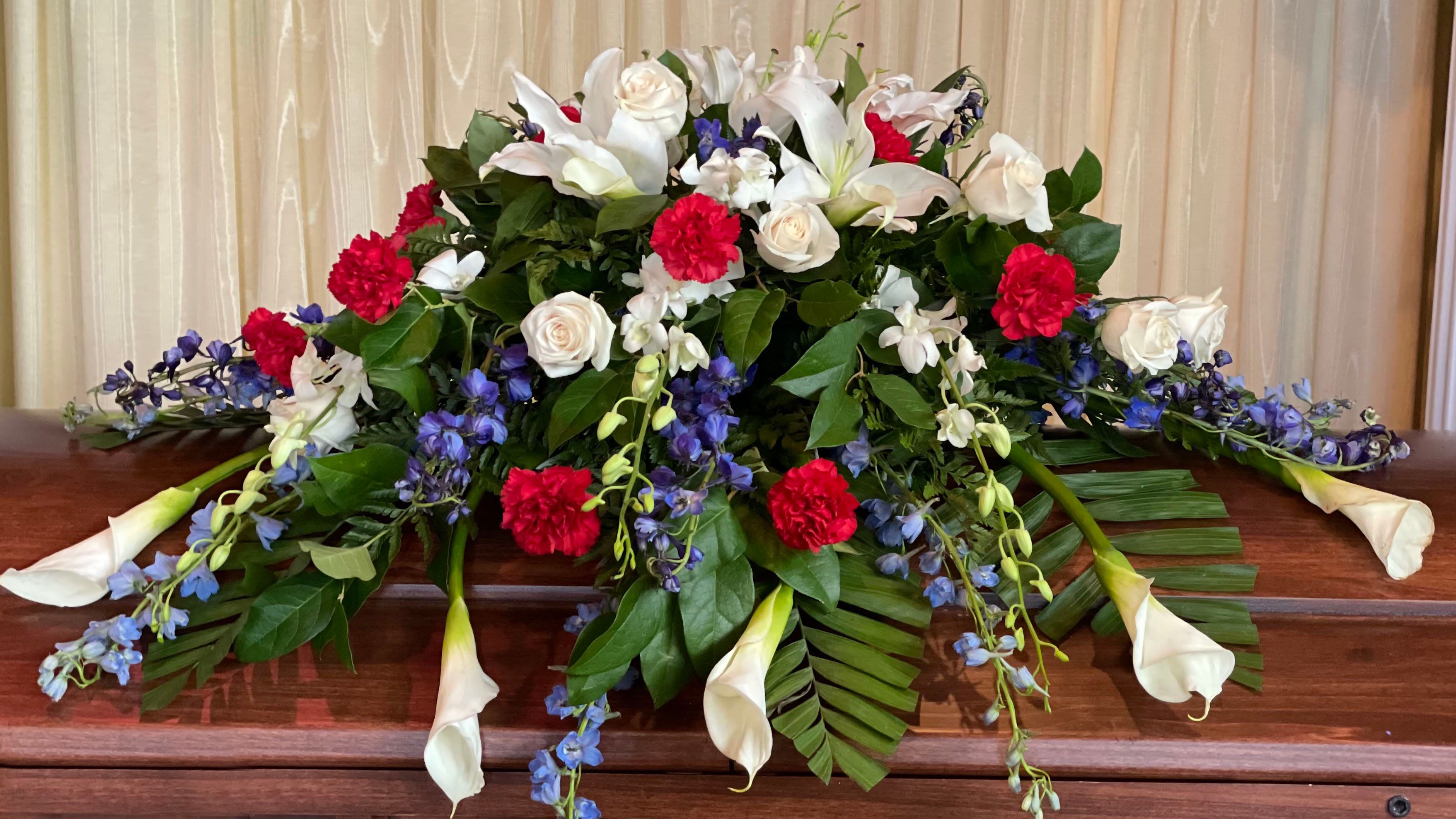Casket spray with white lilies, roses, red carnations, and blue flowers