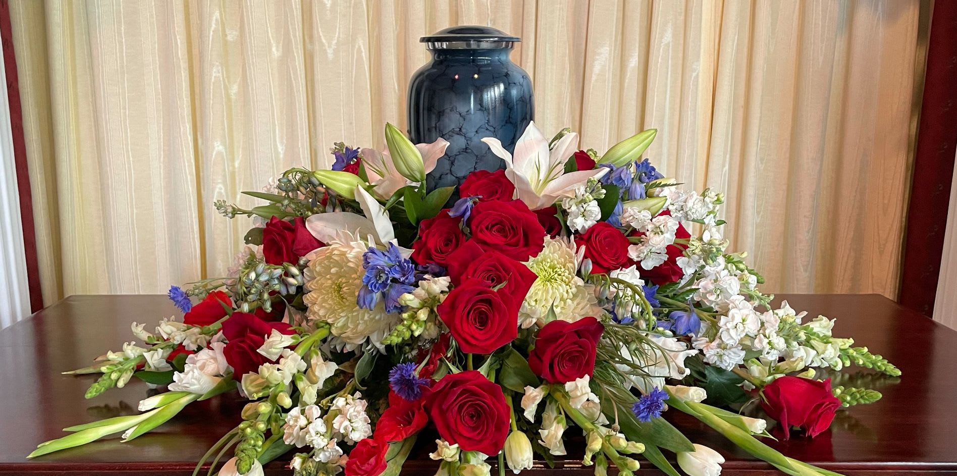 Large floral arrangement with red roses, white lilies, and blue flowers in a blue vase