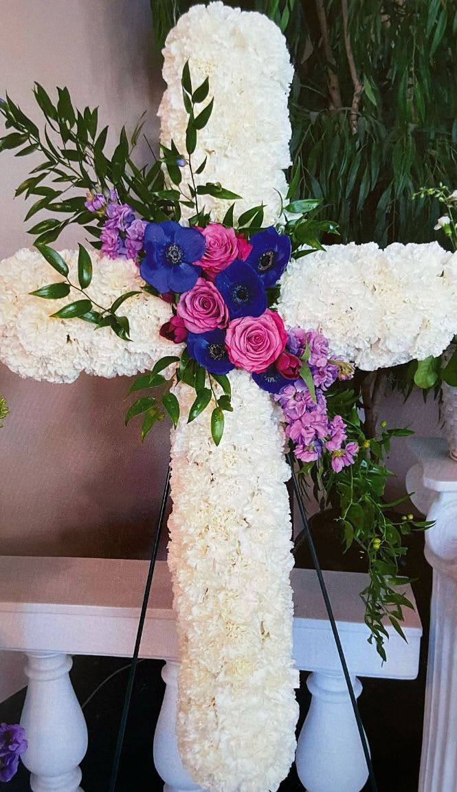 White floral cross on an easel with pink and blue flowers at the center