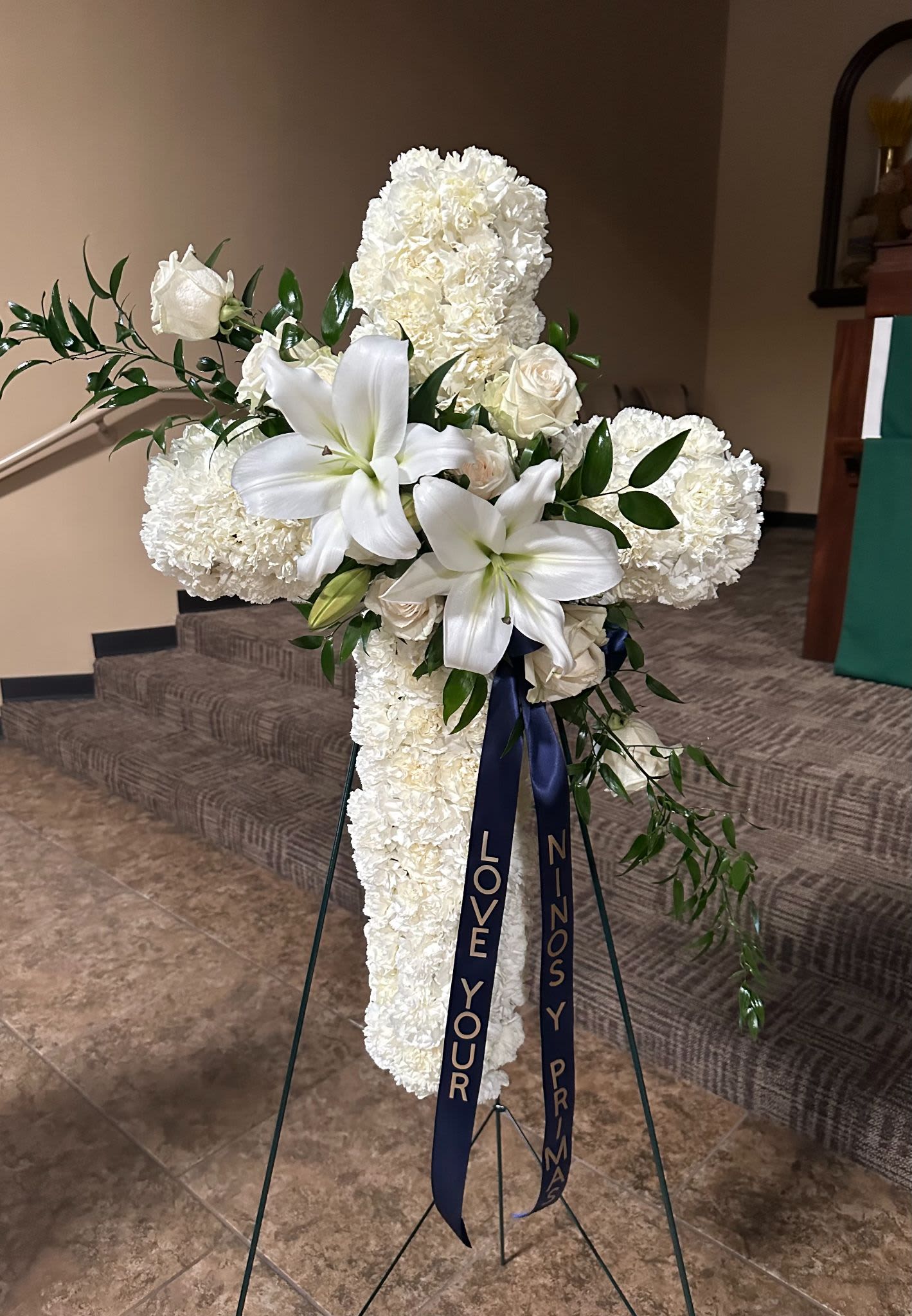 White floral cross on a stand with ribbon streamers
