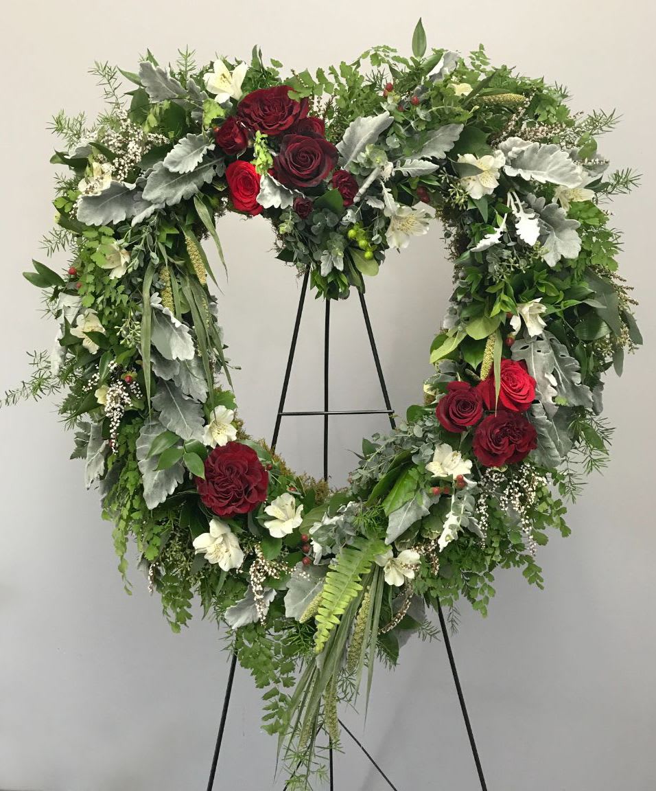 Heart-shaped floral wreath with red roses and white flowers on a stand