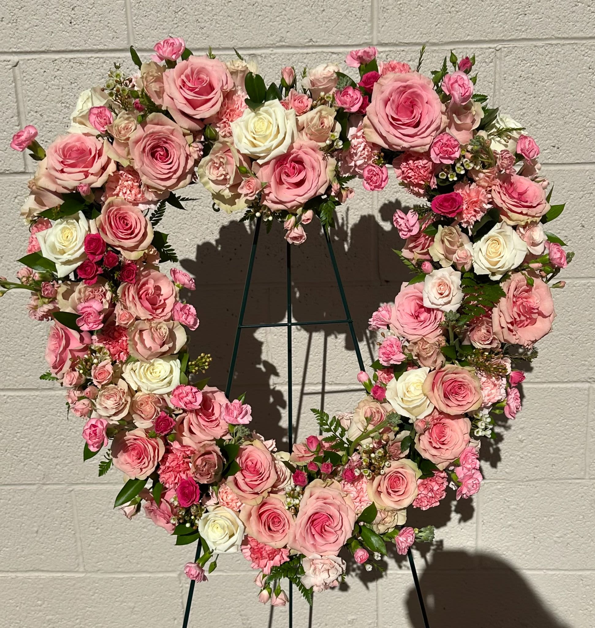 Heart-shaped floral wreath of pink and white roses on a stand