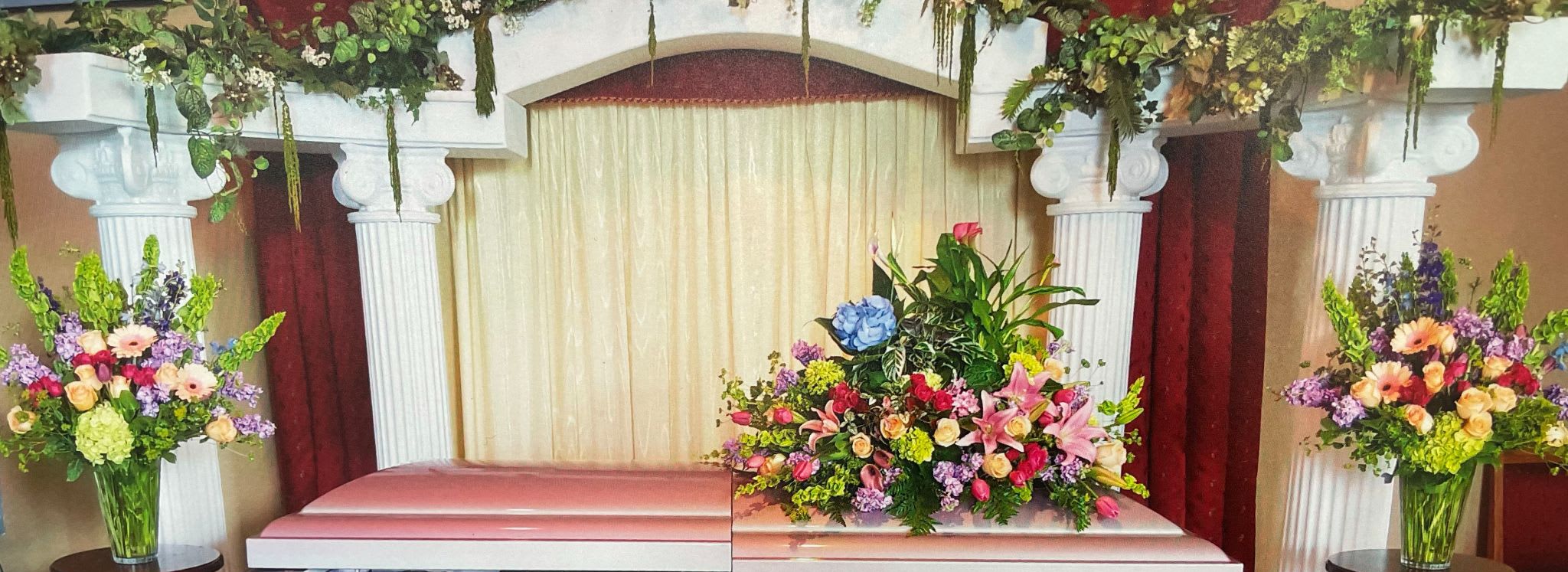 Floral arrangements with pink, purple, and white flowers on a stage with columns