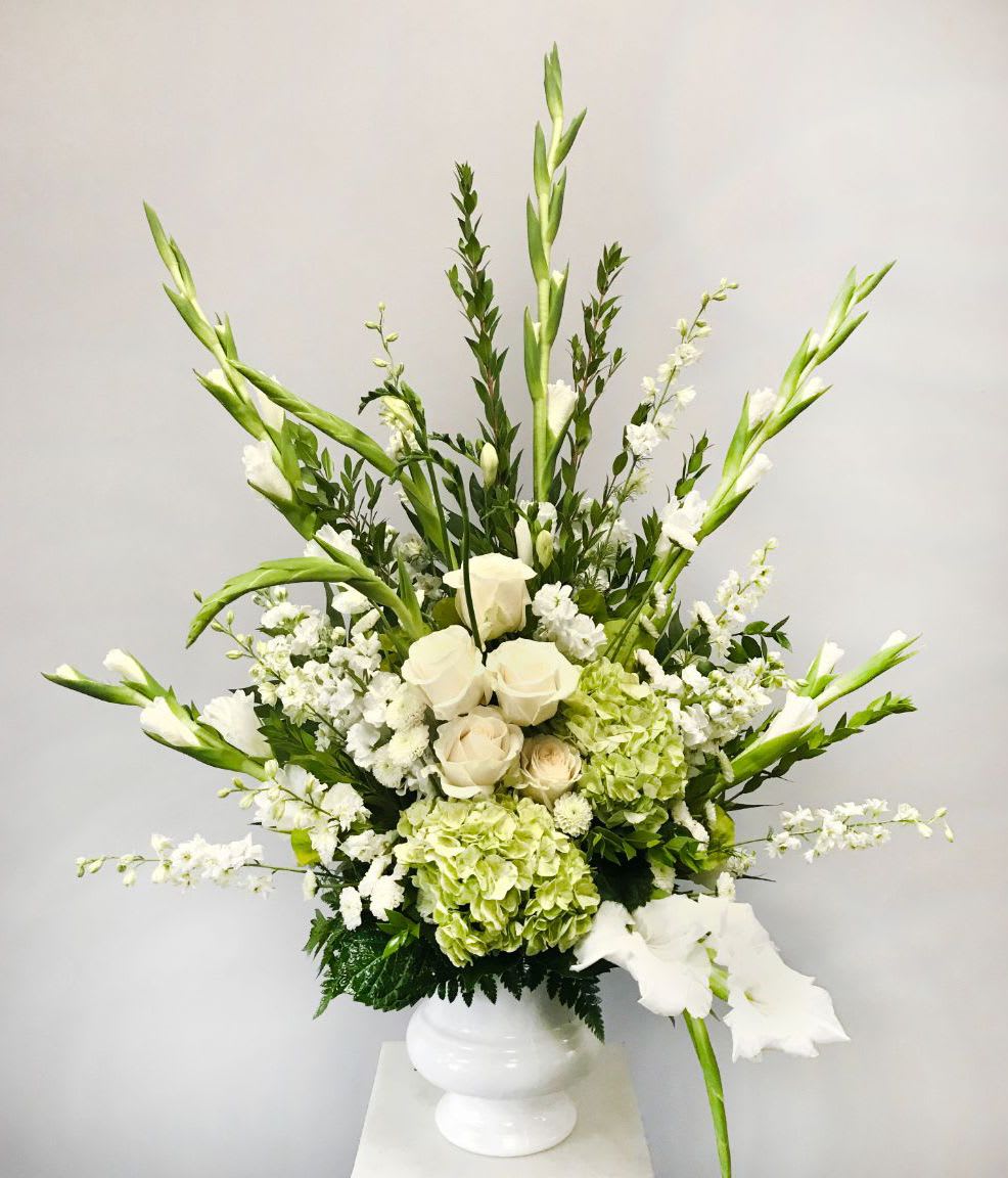Tall white and green arrangement with roses, hydrangeas and gladiolus in a white pedestal vase