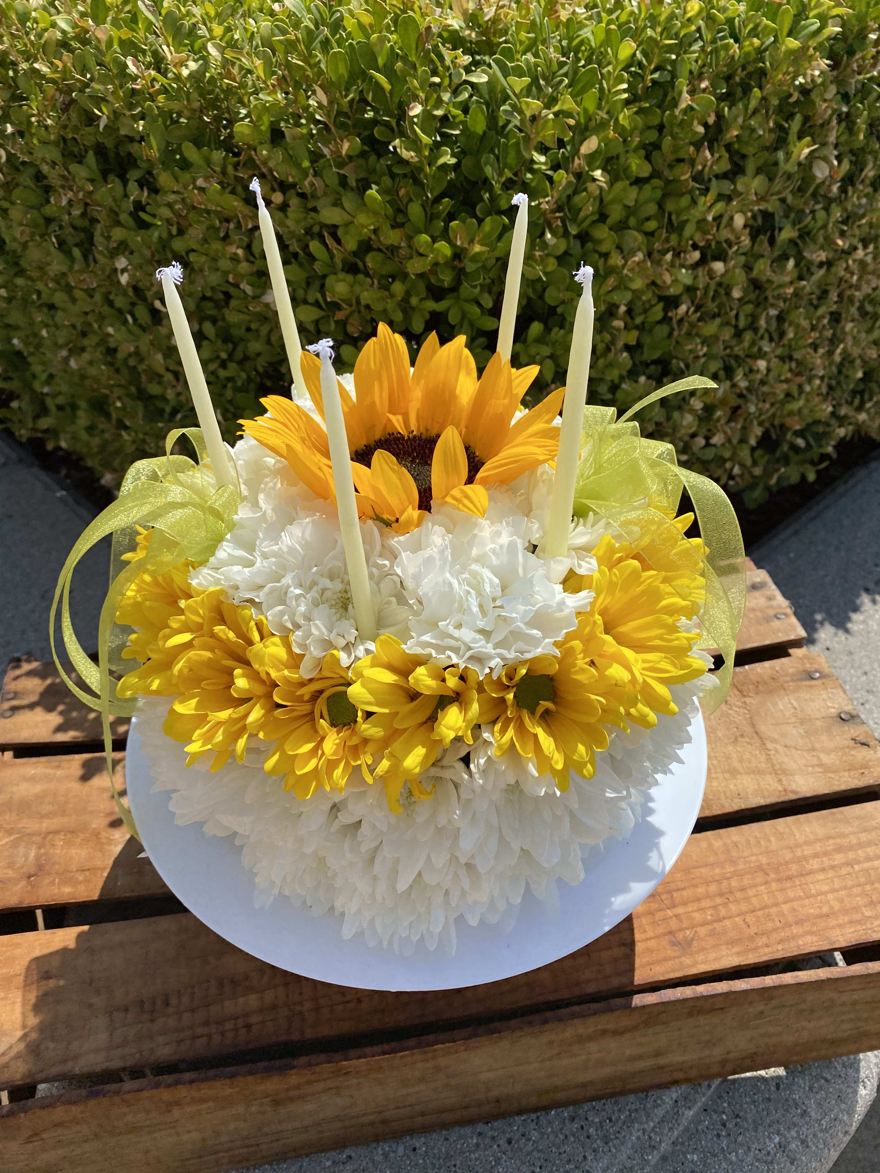 Life of the Party  - Say "Happy Birthday!" with this one of a kind floral cake. White mums, carnations, and yellow daisies make up this charming cake and is topped with a beautiful sunflower, bows and birthday candles. we have same-day flower delivery available 
