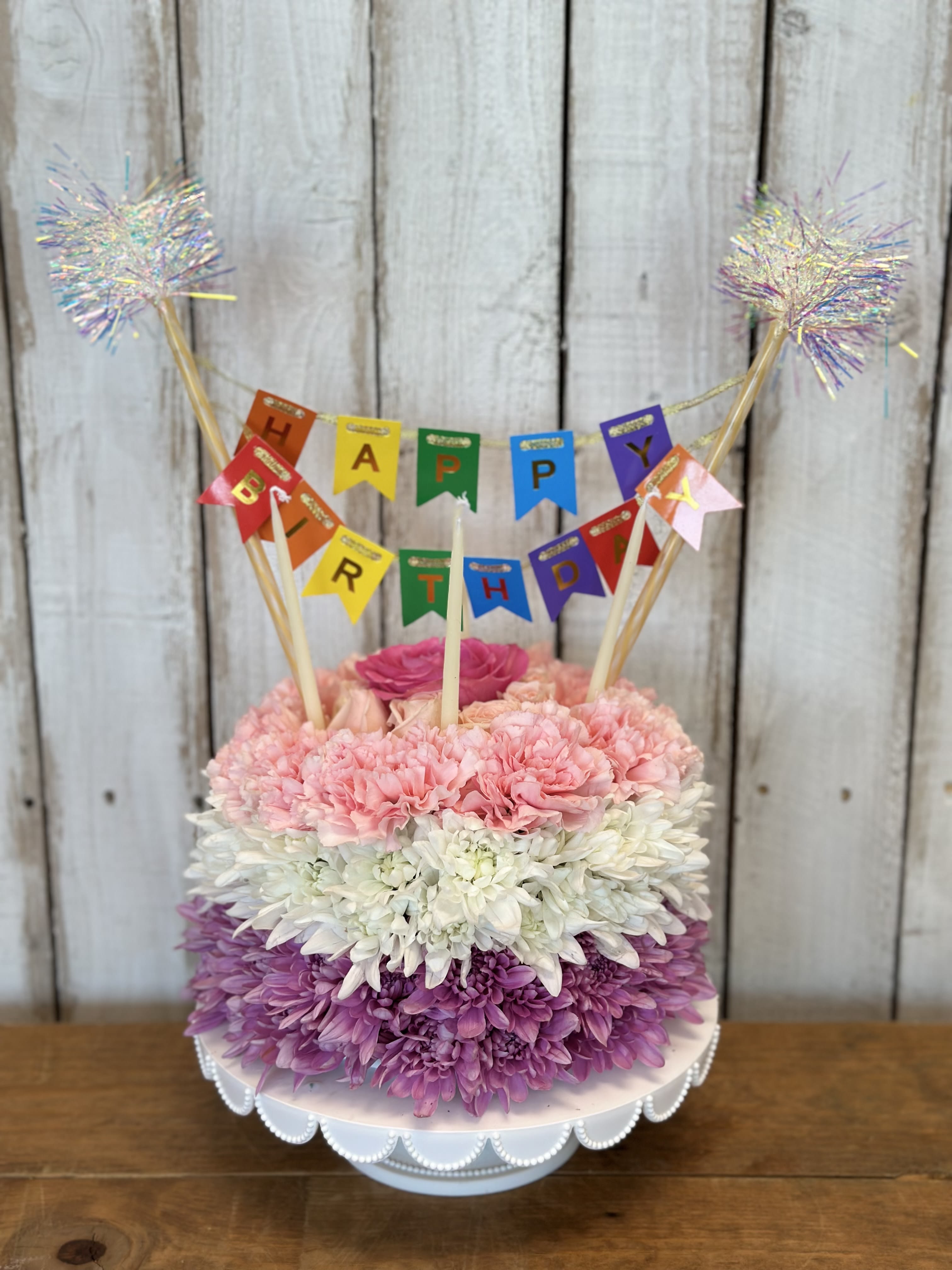 Birthday cake made of pink, white, and purple flowers with a banner topper