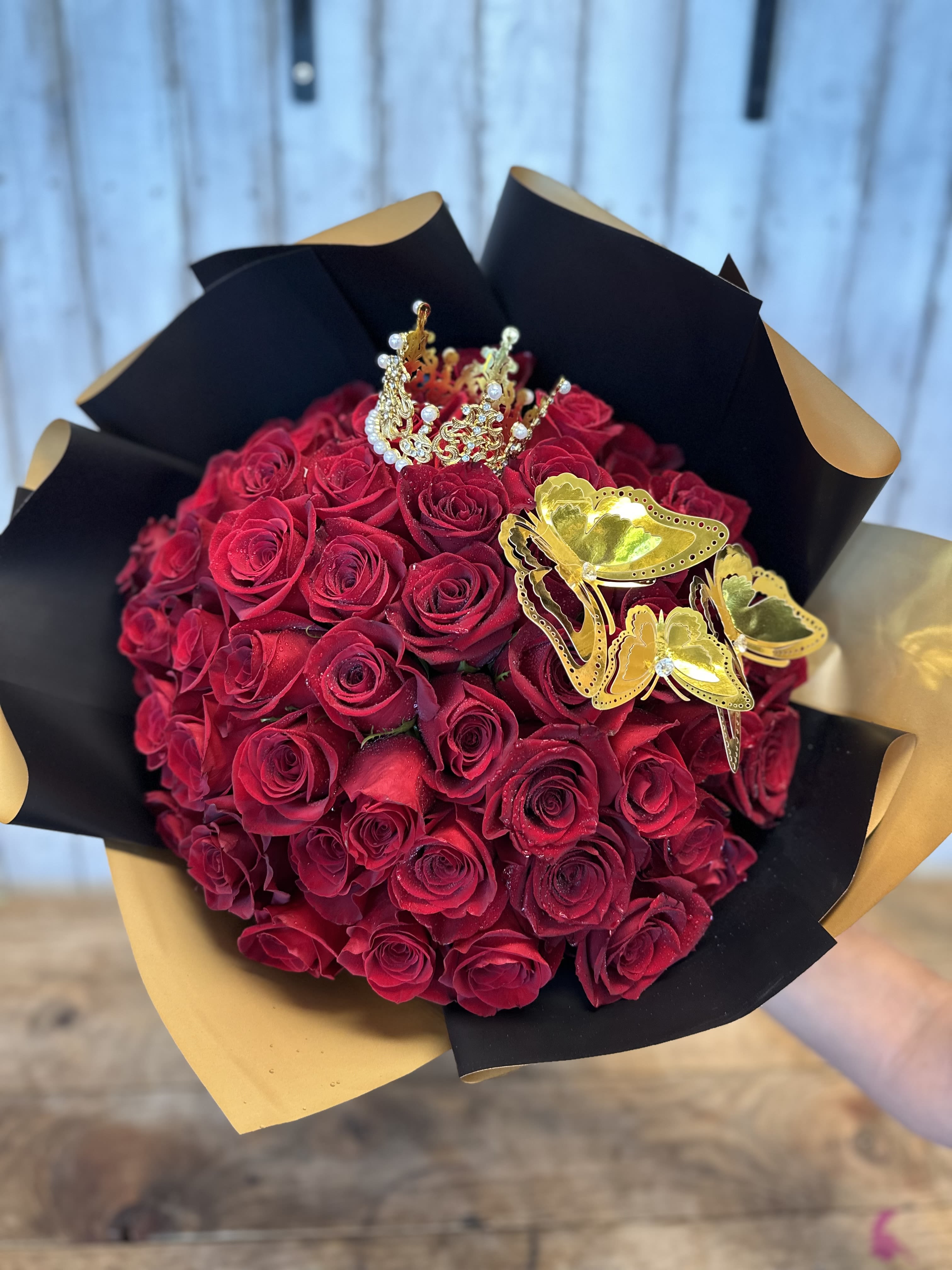Queen Butterfly Ramo Buchón - Queen Butterfly Ramo Buchón Turn heads with this luxurious red rose Ramo Buchón designed to make a bold and unforgettable statement. Featuring dozens of premium deep red roses wrapped in elegant black and nude waterproof paper, this bouquet is finished with a sparkling crown and gold butterfly accents for the ultimate princess vibe. Perfect for birthdays, anniversaries, graduations, proposals, Valentine’s Day, or just because. Our handcrafted Ramo Buchón bouquets are designed with fresh, farm-direct roses for maximum beauty, fullness, and long-lasting freshness. This trendy luxury bouquet is ideal for anyone who loves dramatic, romantic floral designs with a modern glam touch. 50 roses 75 roses 100 roses 