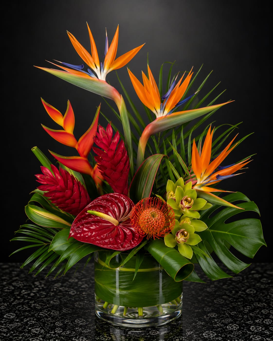 Tropical arrangement with bird of paradise, anthurium, and orchids in a glass vase