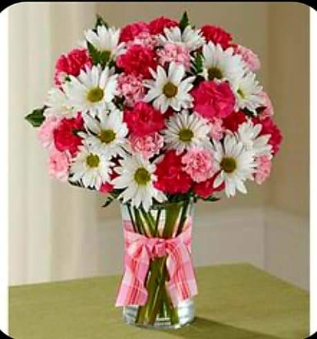 Bouquet of white daisies and pink carnations in a glass vase with a pink ribbon