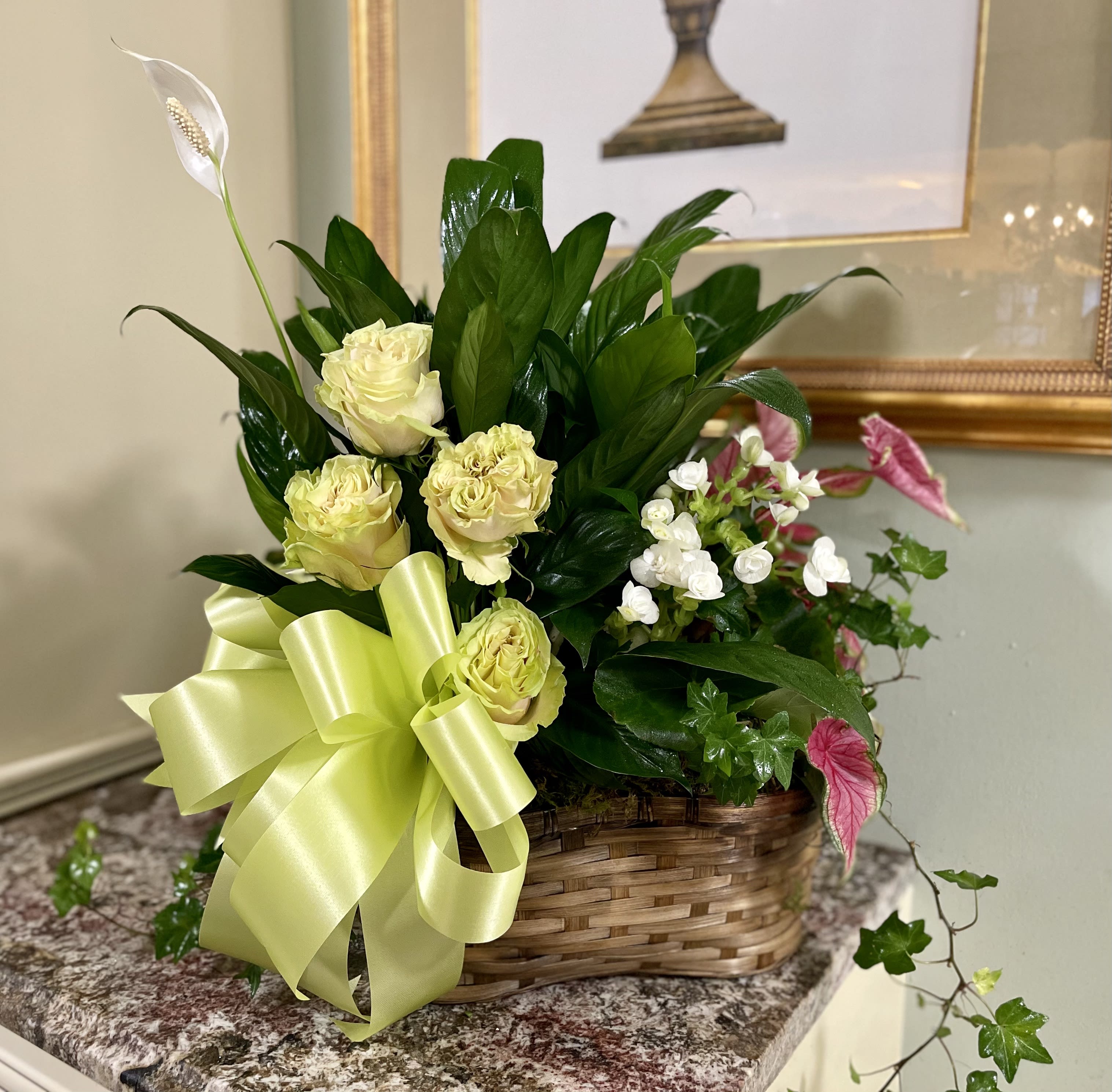 Basket arrangement of pale yellow roses with white blooms and a large ribbon
