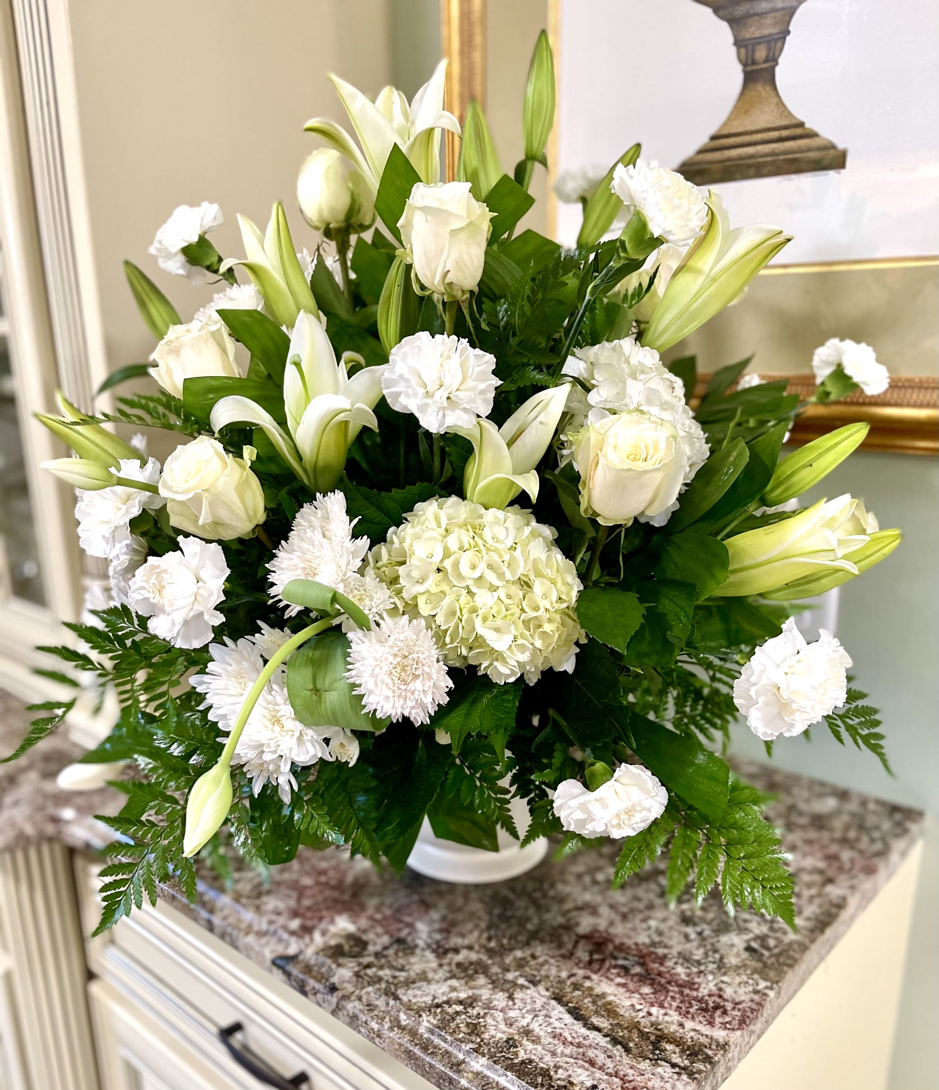 White floral arrangement with lilies, roses, hydrangea, and carnations in a vase