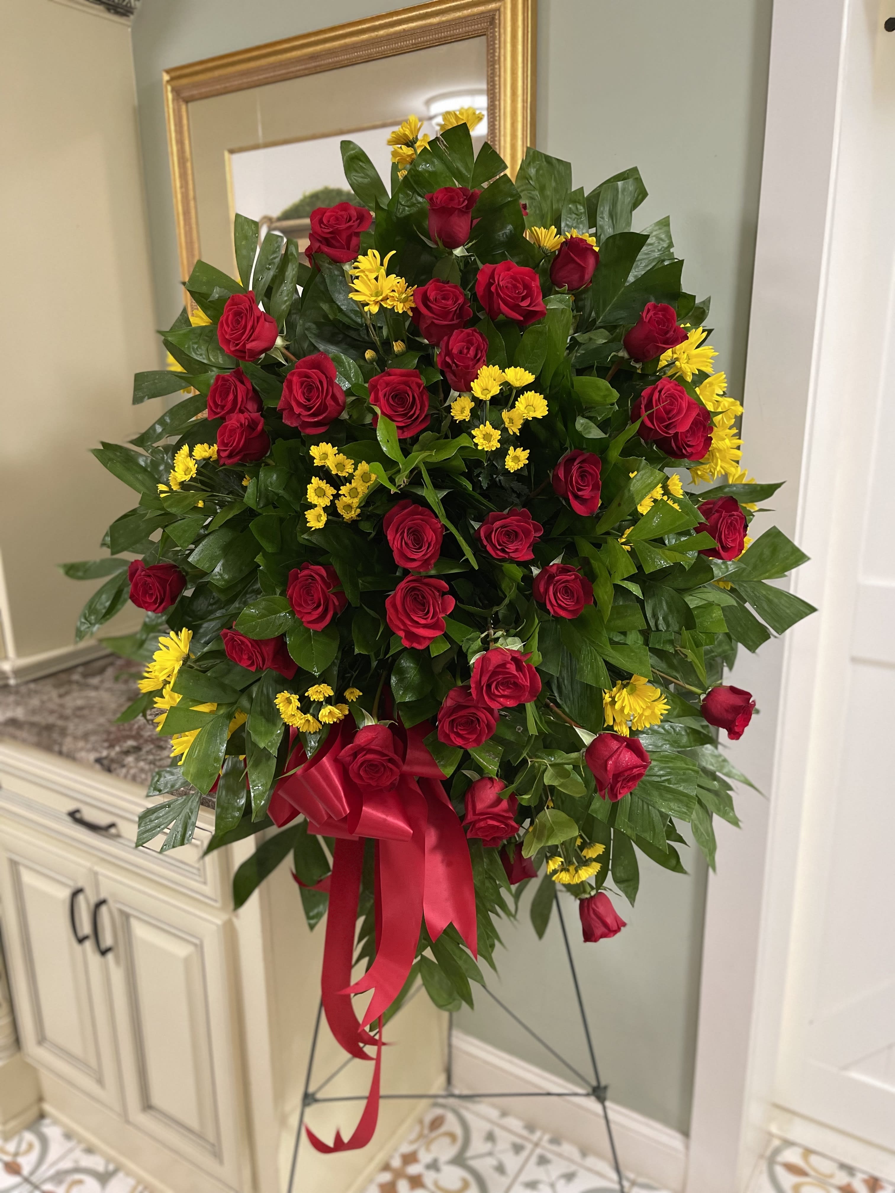 Standing spray of red roses and yellow daisies with a red ribbon
