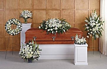 White funeral casket surrounded by white floral sprays and wreaths