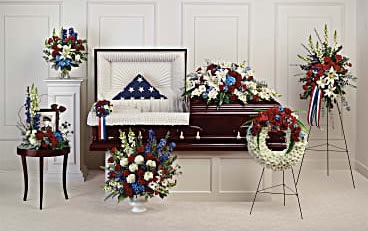Patriotic funeral floral set with red, white, and blue arrangements around a casket