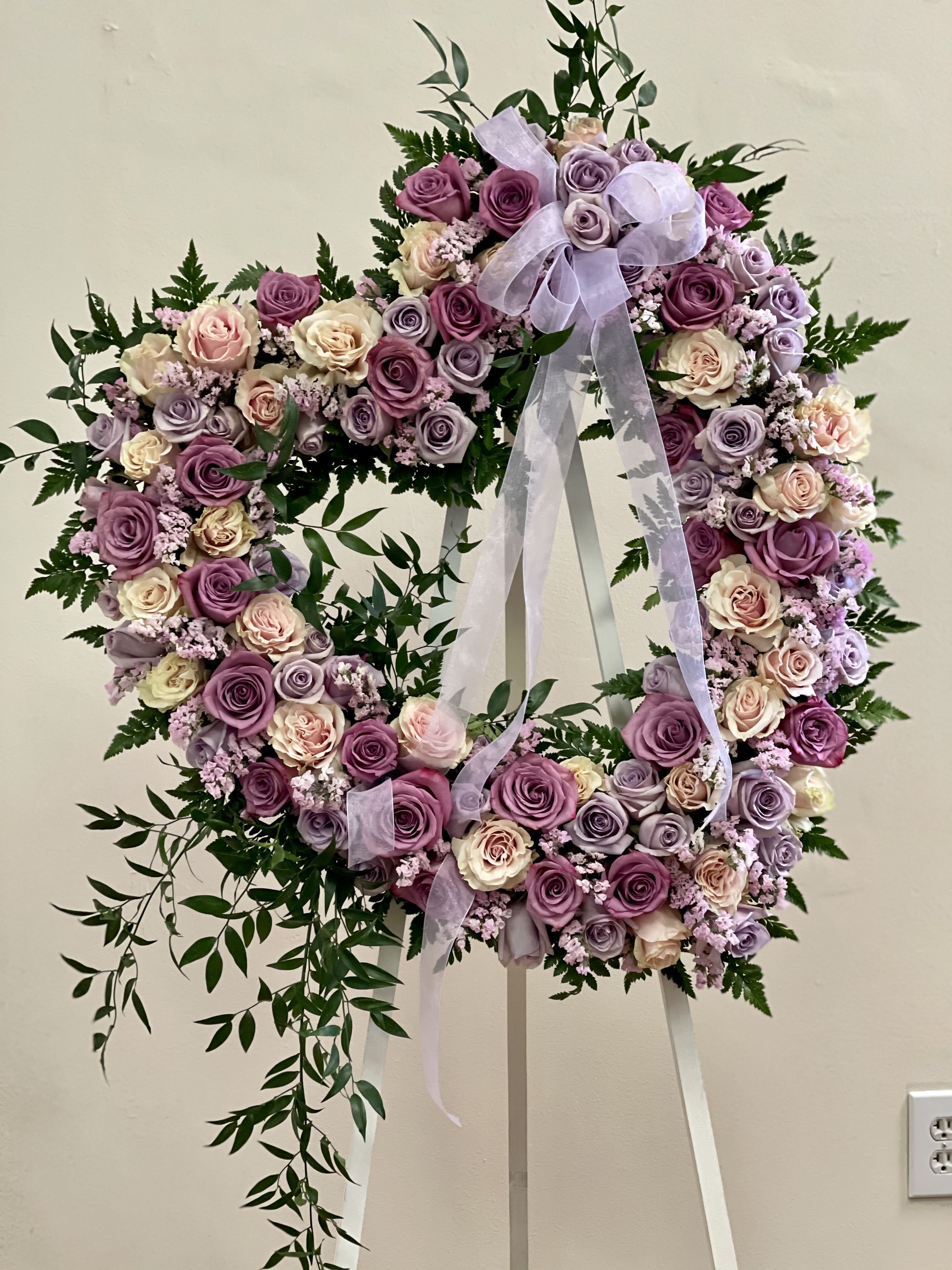 Heart-shaped wreath of pink and lavender roses on a white stand with ribbon