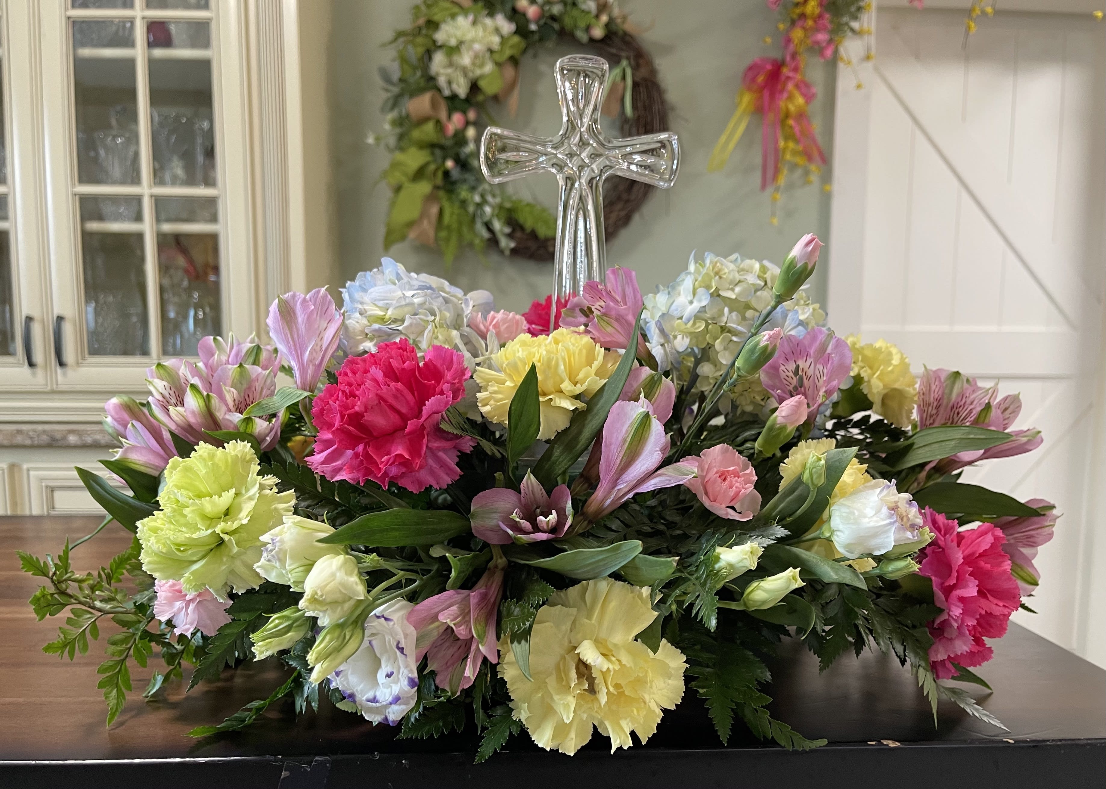 Colorful floral casket spray with a clear glass cross centerpiece