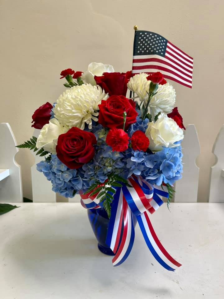 Red and white roses with blue hydrangeas in a vase, topped with an American flag