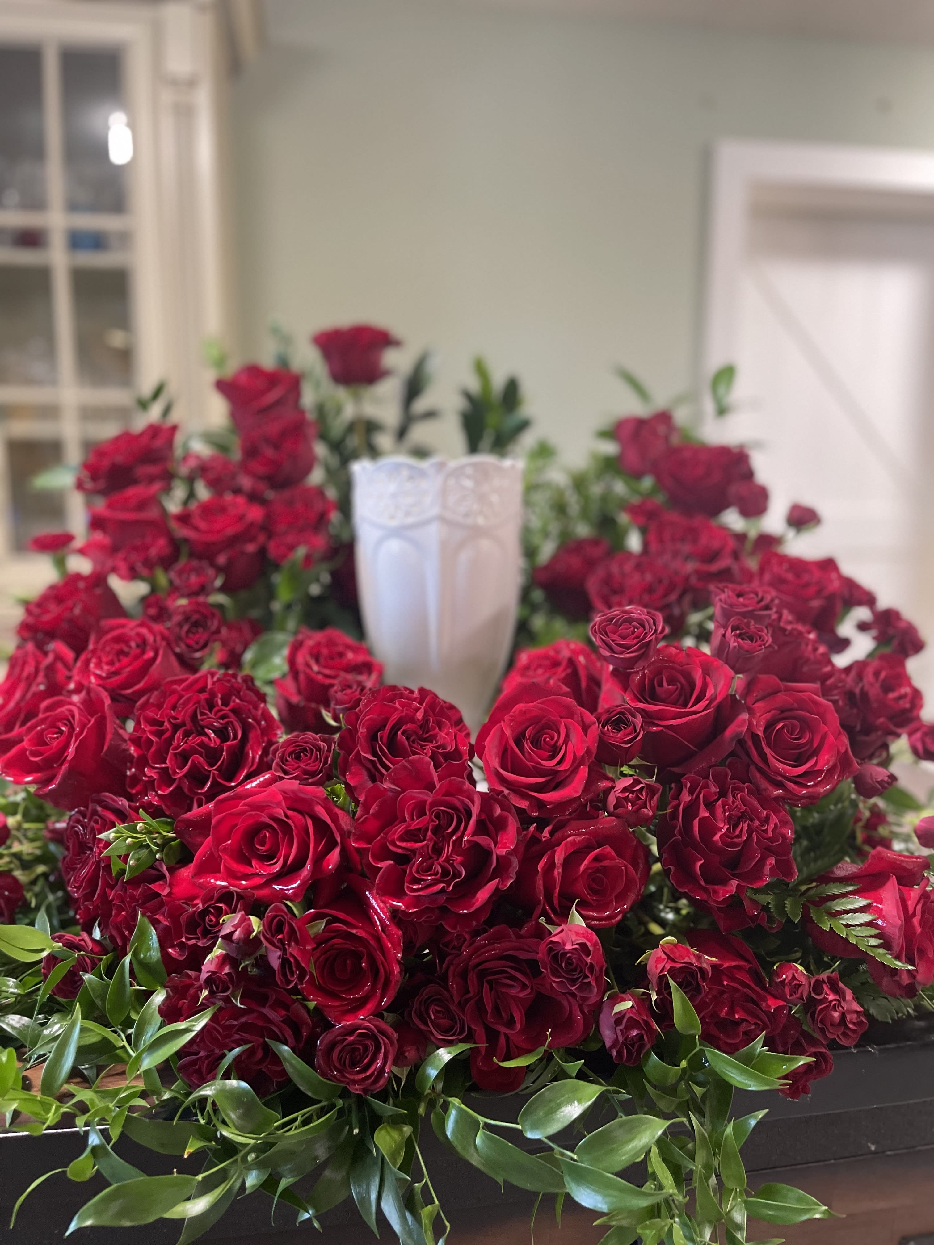 Red rose arrangement surrounding a white urn centerpiece