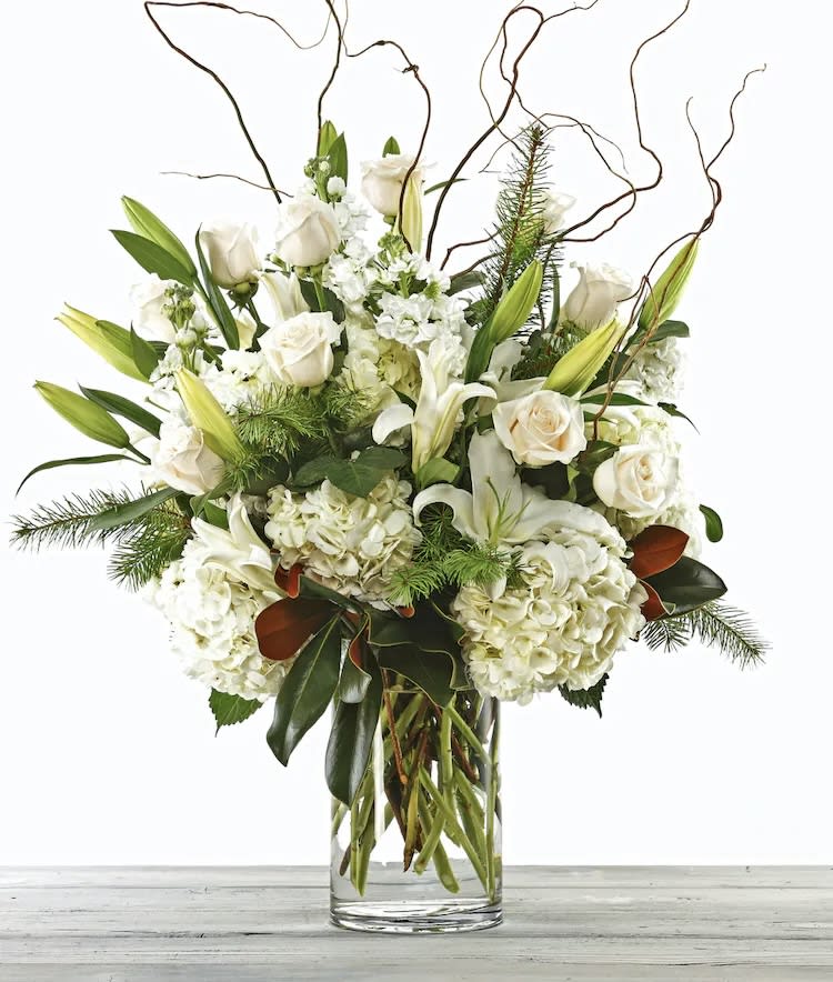 White roses and lilies in a clear glass vase with curly branches