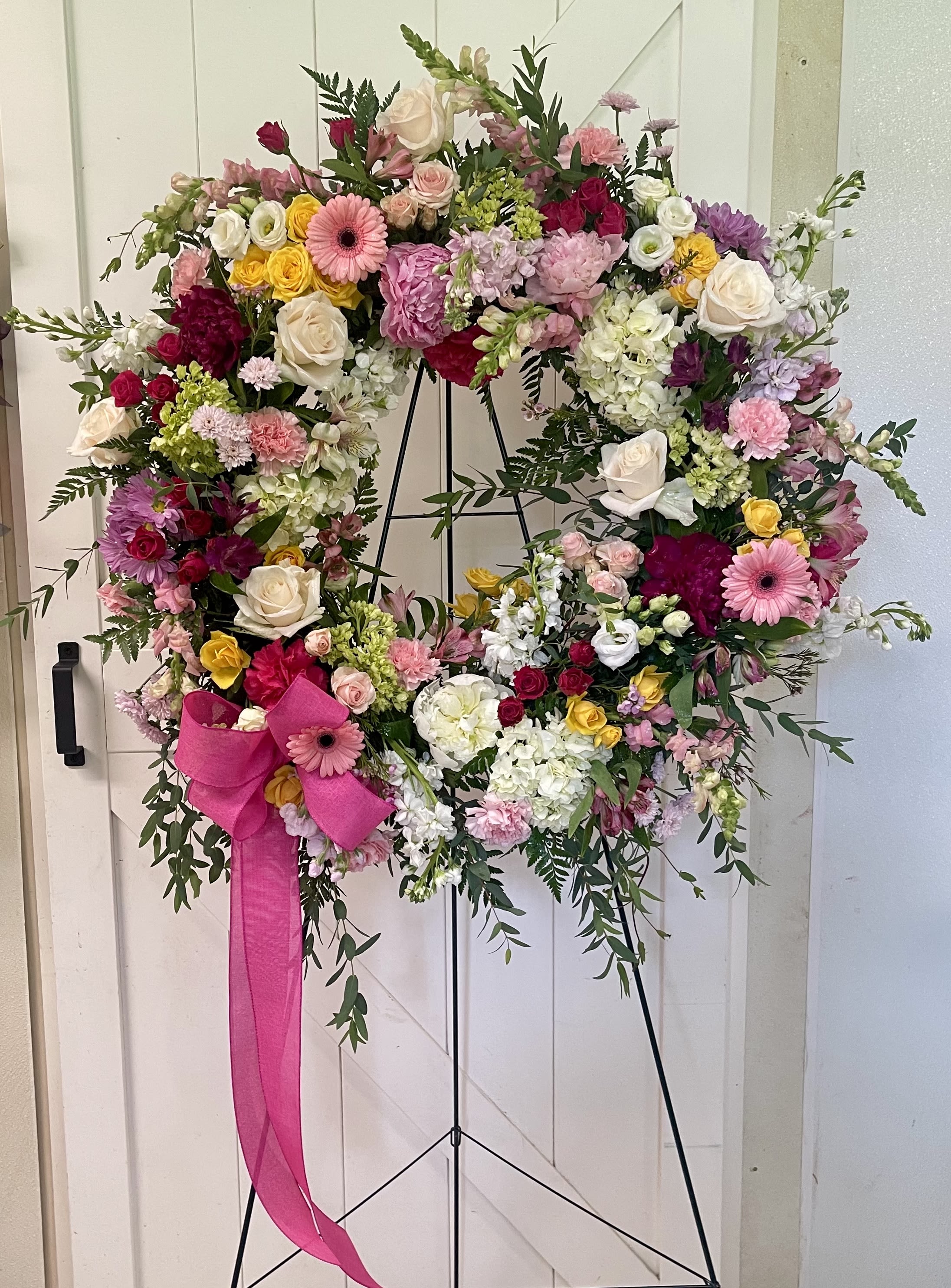Large floral wreath on a black stand with a pink ribbon