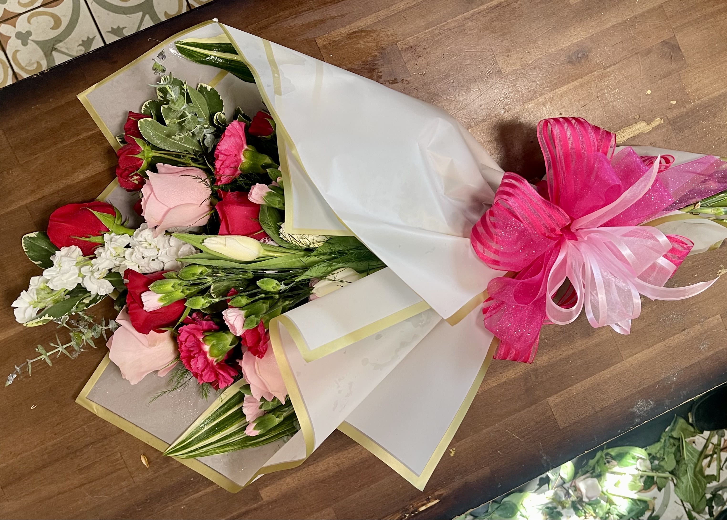 Bouquet of red and pink roses wrapped in white paper with a pink ribbon