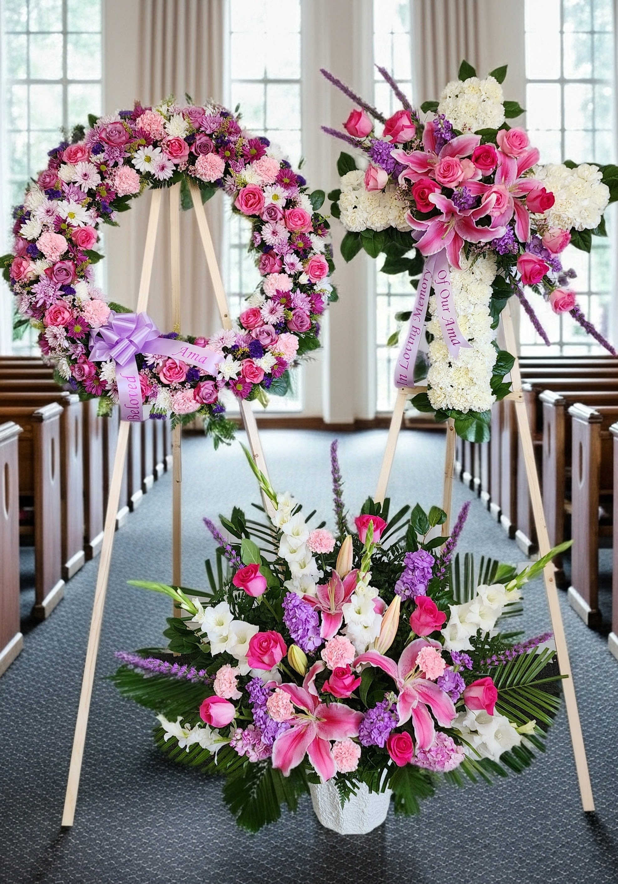 Three pink and white floral funeral tributes on easels in a church aisle