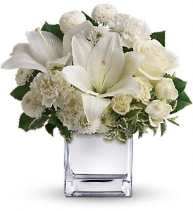 White lilies and cream flowers arranged in a clear square vase