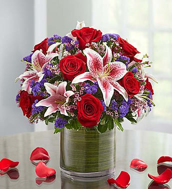Red roses and pink lilies in a glass vase with purple filler flowers