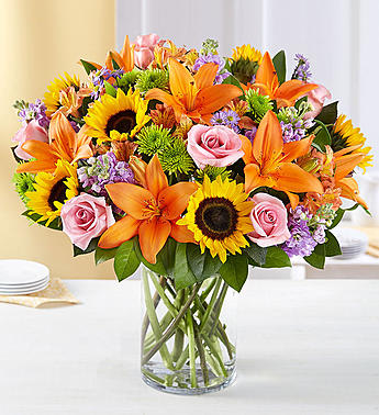 Mixed bouquet of sunflowers, orange lilies, and pink roses in a glass vase