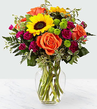 Mixed bouquet with sunflowers, orange roses, and magenta blooms in a glass vase