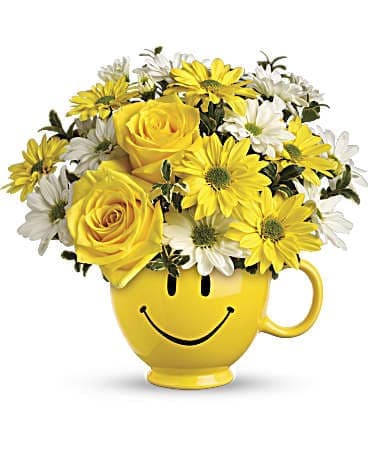 Yellow mug with a smiley face holding yellow roses and white daisies