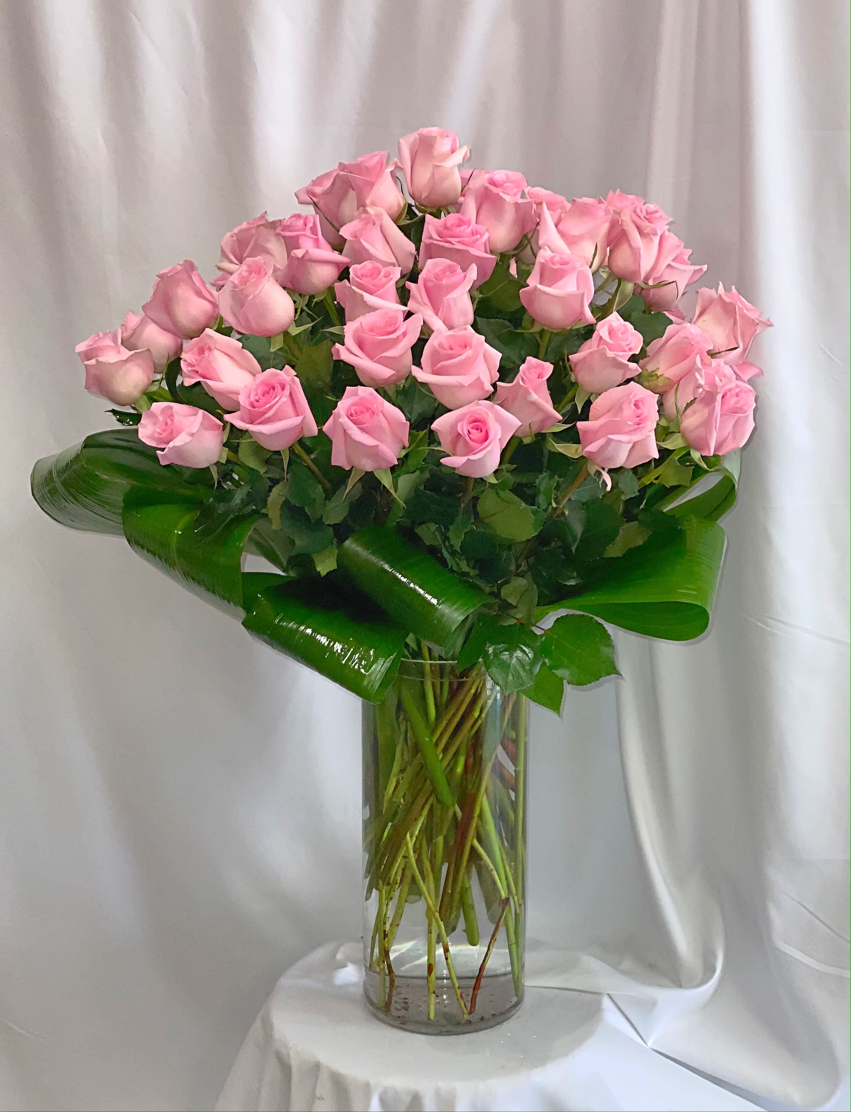 Pink roses arranged in a tall clear glass vase with broad green leaves