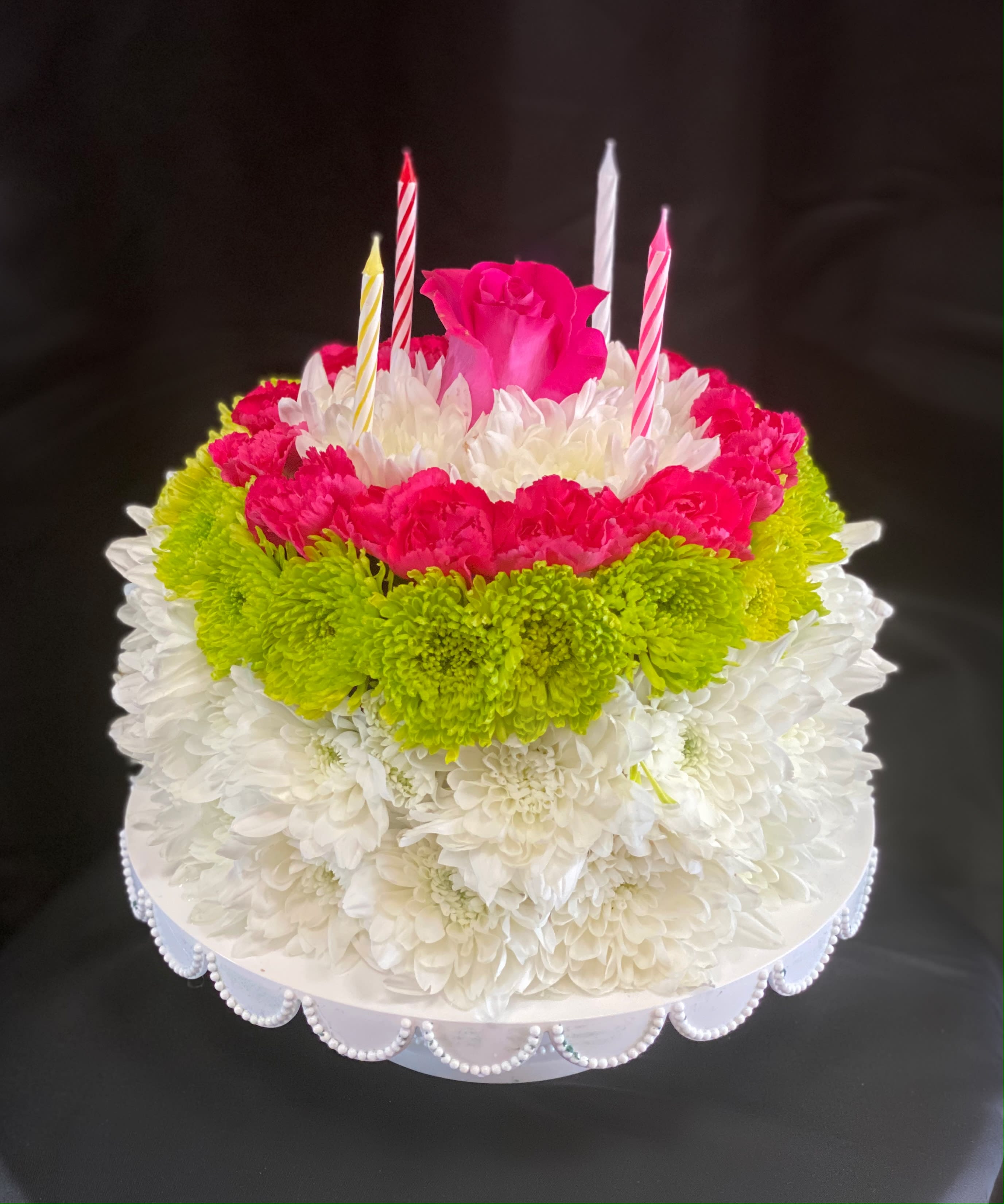 Round floral cake with pink, white, and green flowers and candles