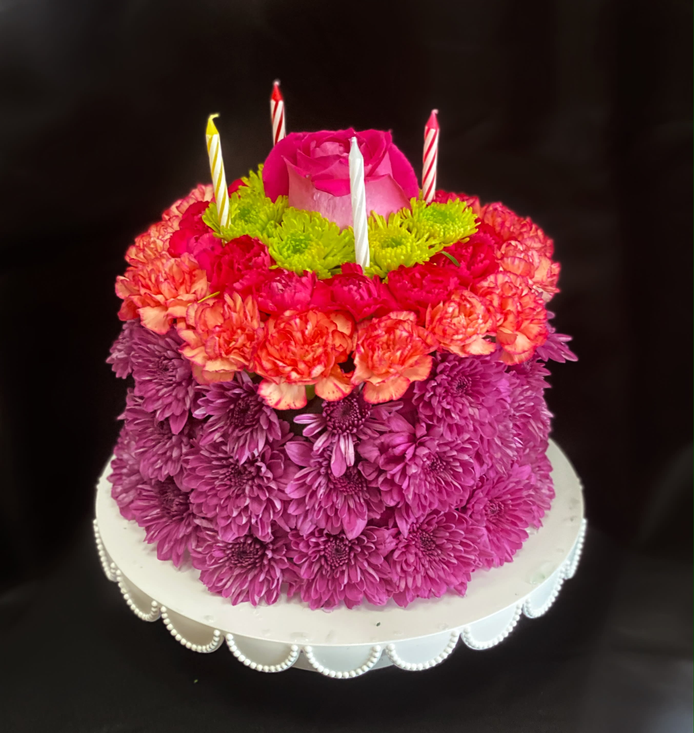 Tiered floral cake with a pink rose topper and striped candles